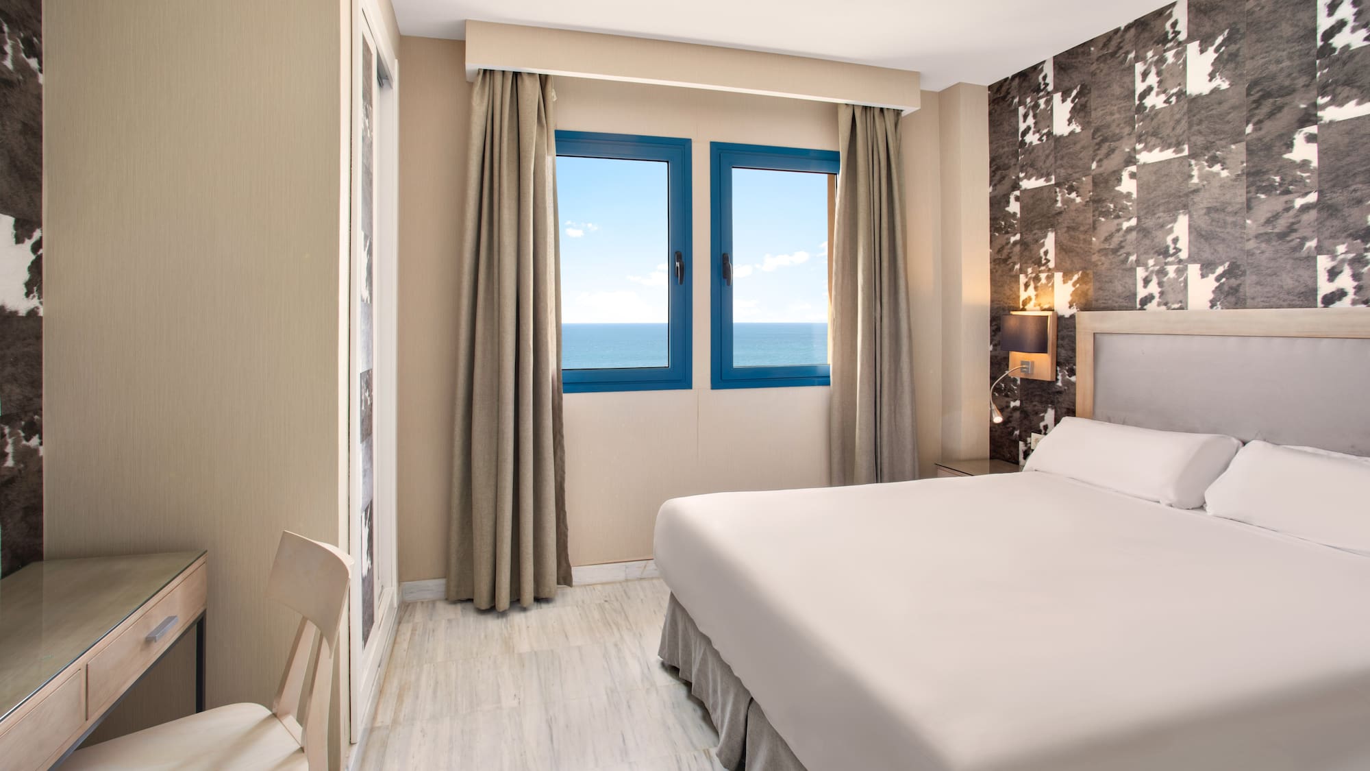 Modern hotel bedroom with sea view, large bed, and desk.