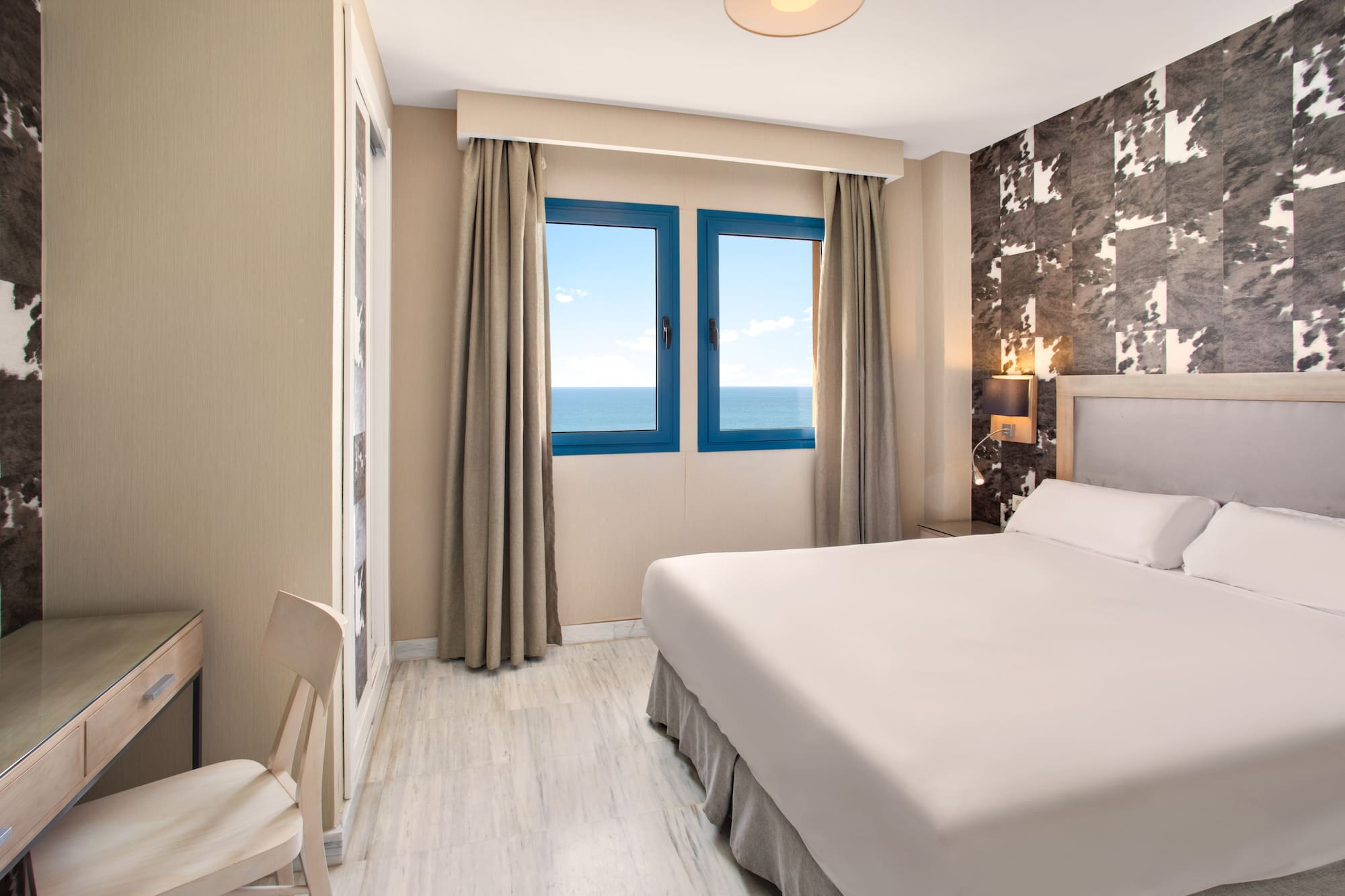 Modern hotel bedroom with sea view, large bed, and desk.
