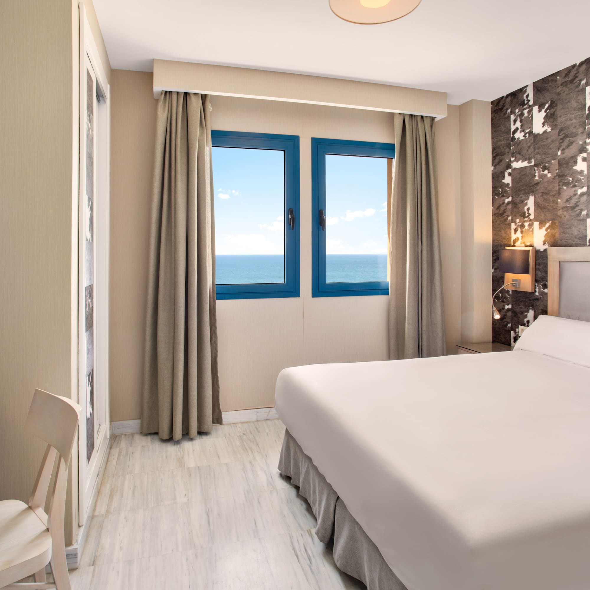 Modern hotel bedroom with sea view, large bed, and desk.