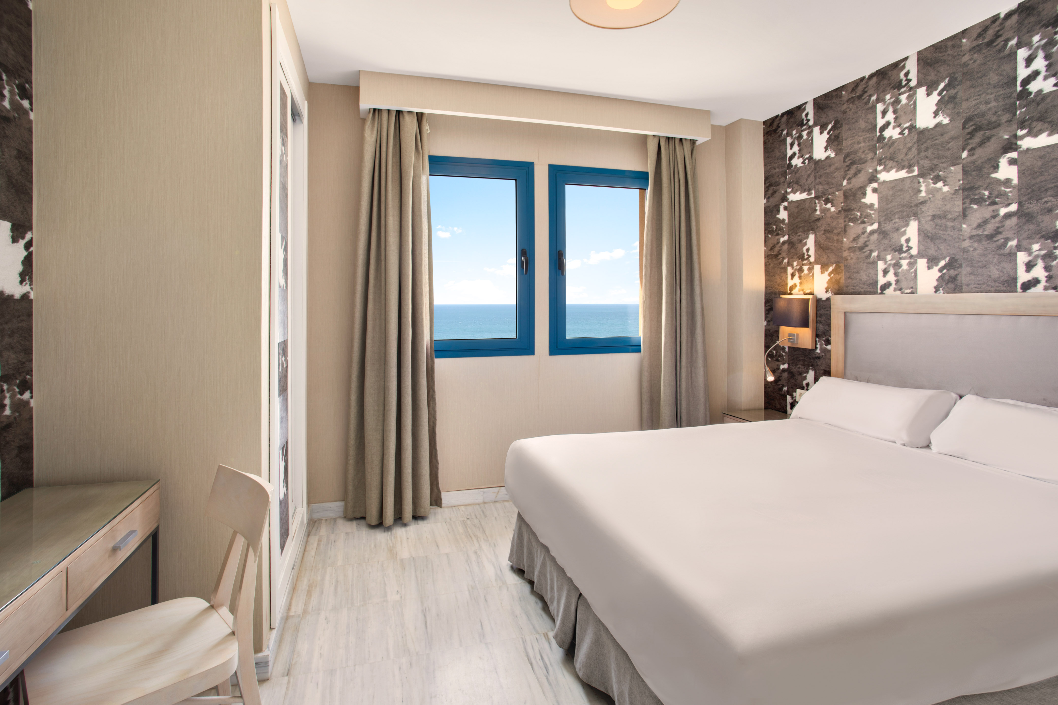 Modern hotel bedroom with sea view, large bed, and desk.