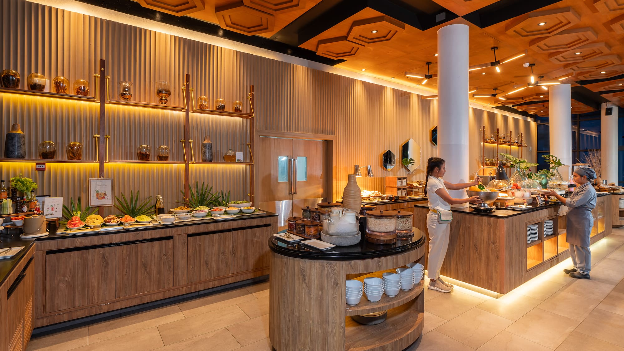 Modern hotel restaurant buffet with staff and varied food, warm wood interior.
