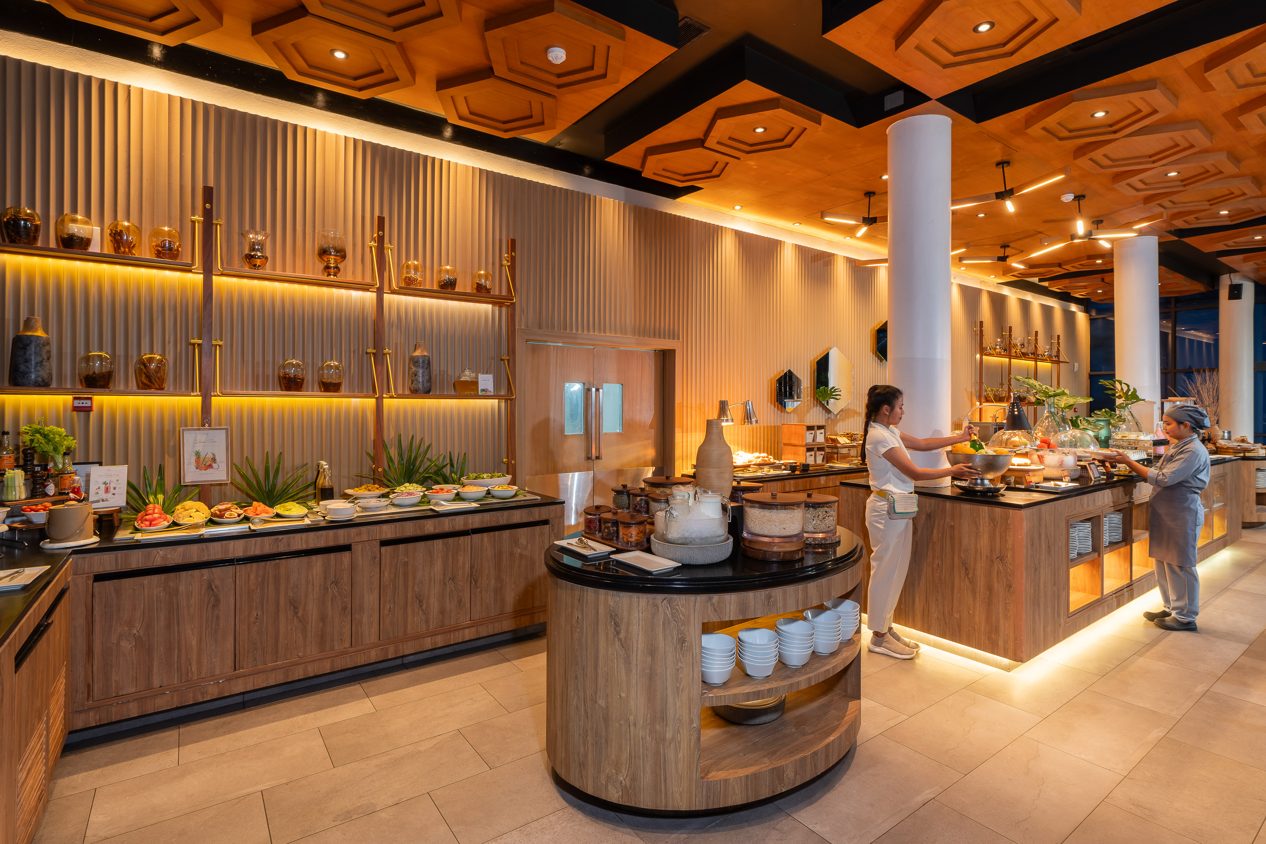 Modern hotel restaurant buffet with staff and varied food, warm wood interior.