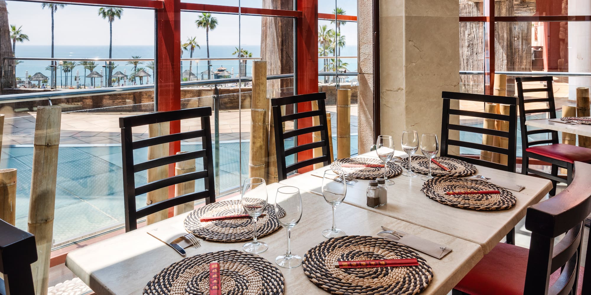 Restaurant with ocean view, palm trees, set tables, and chopsticks.