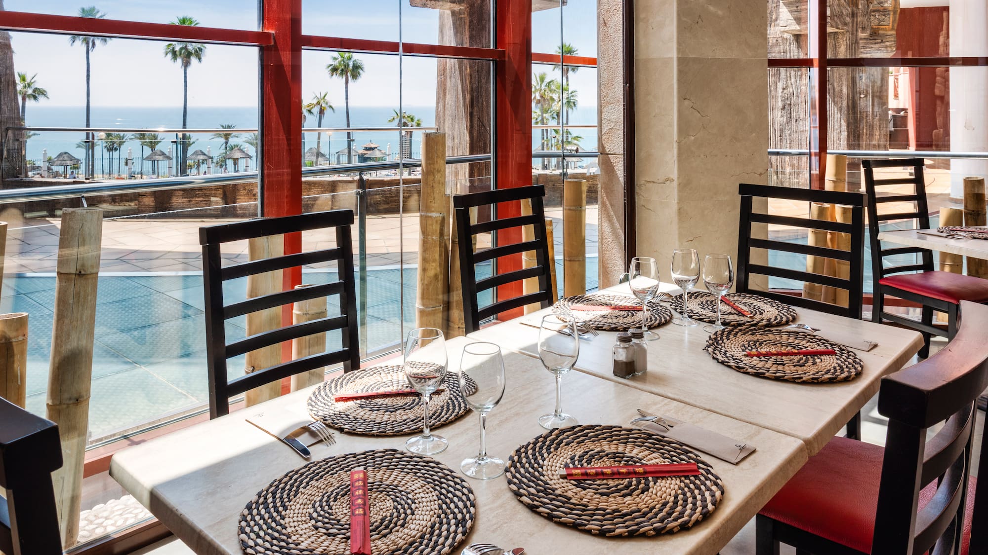 Restaurant with ocean view, palm trees, set tables, and chopsticks.