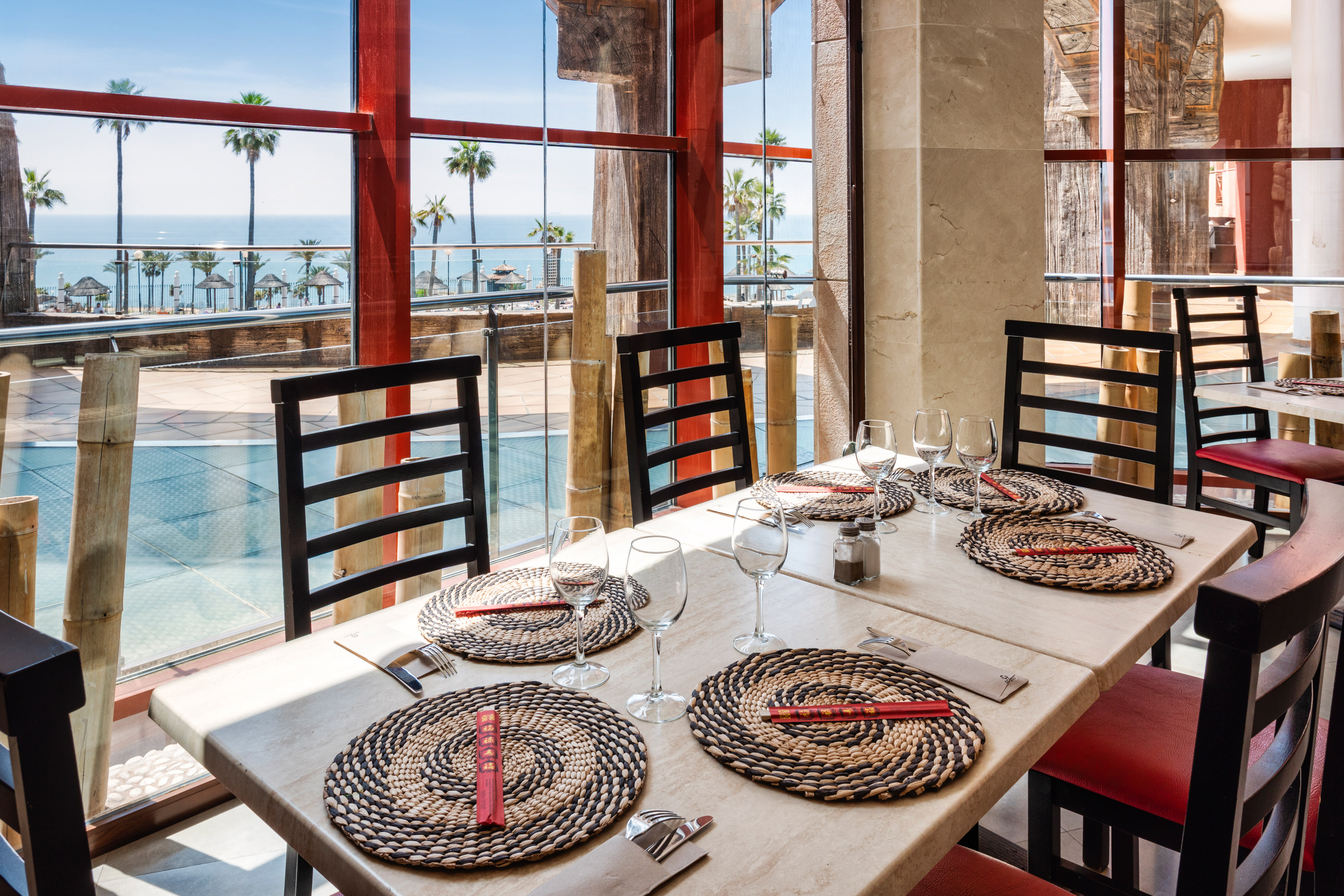 Restaurant with ocean view, palm trees, set tables, and chopsticks.