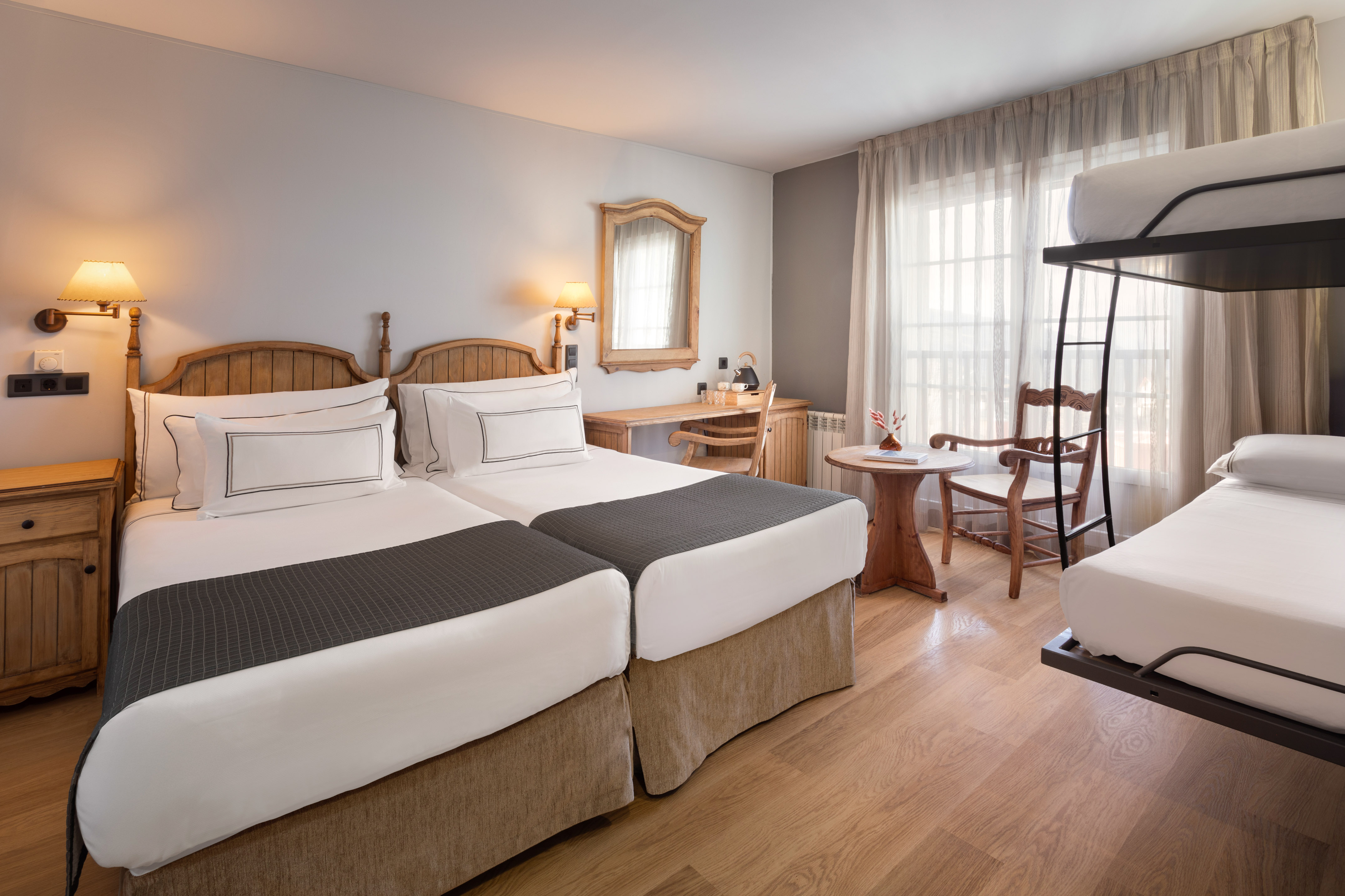 Hotel room with twin beds, bunk bed, wooden desk, and wood floor.
