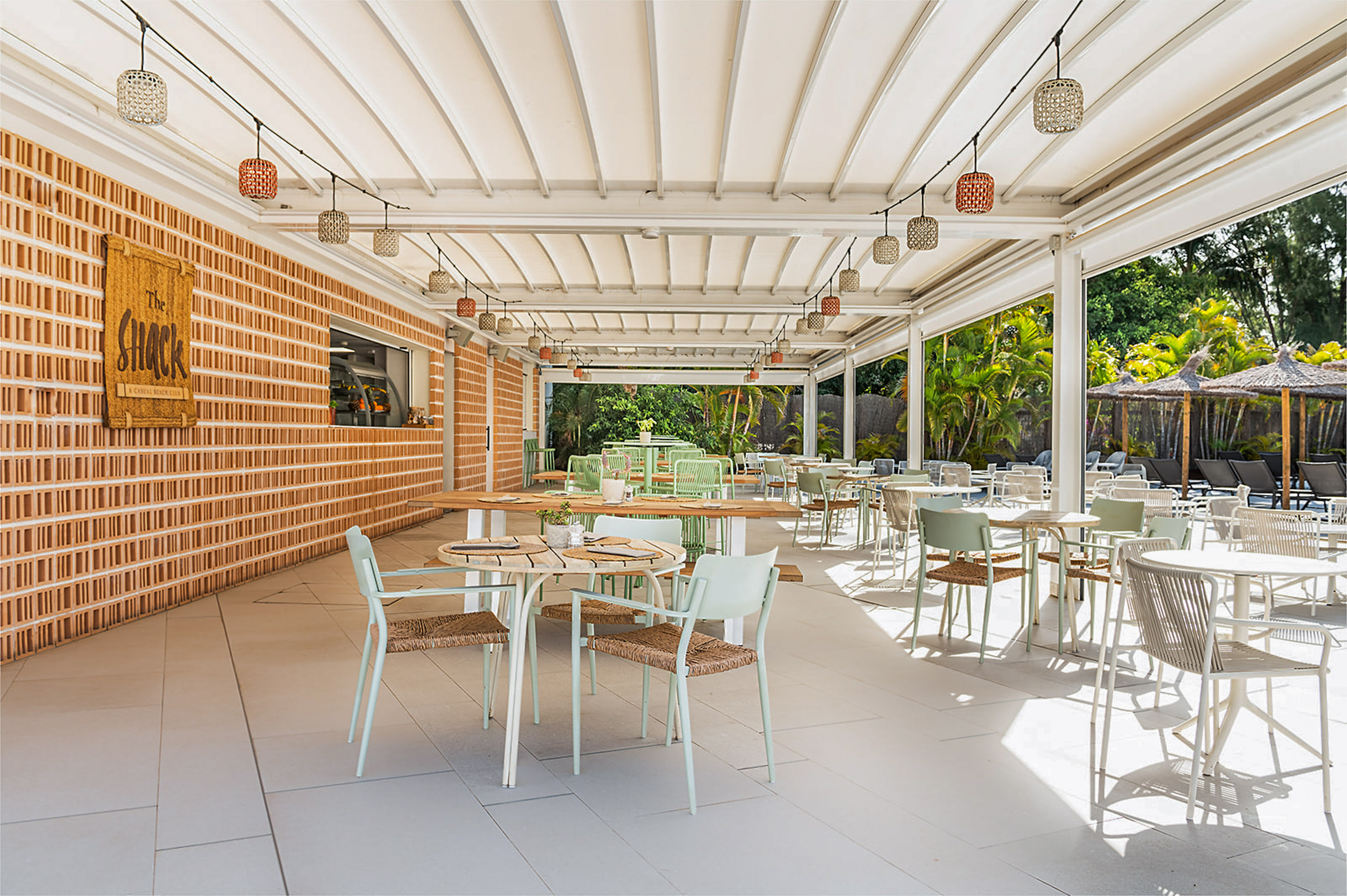 Bright outdoor restaurant with canopy, modern seating, and lush poolside view.