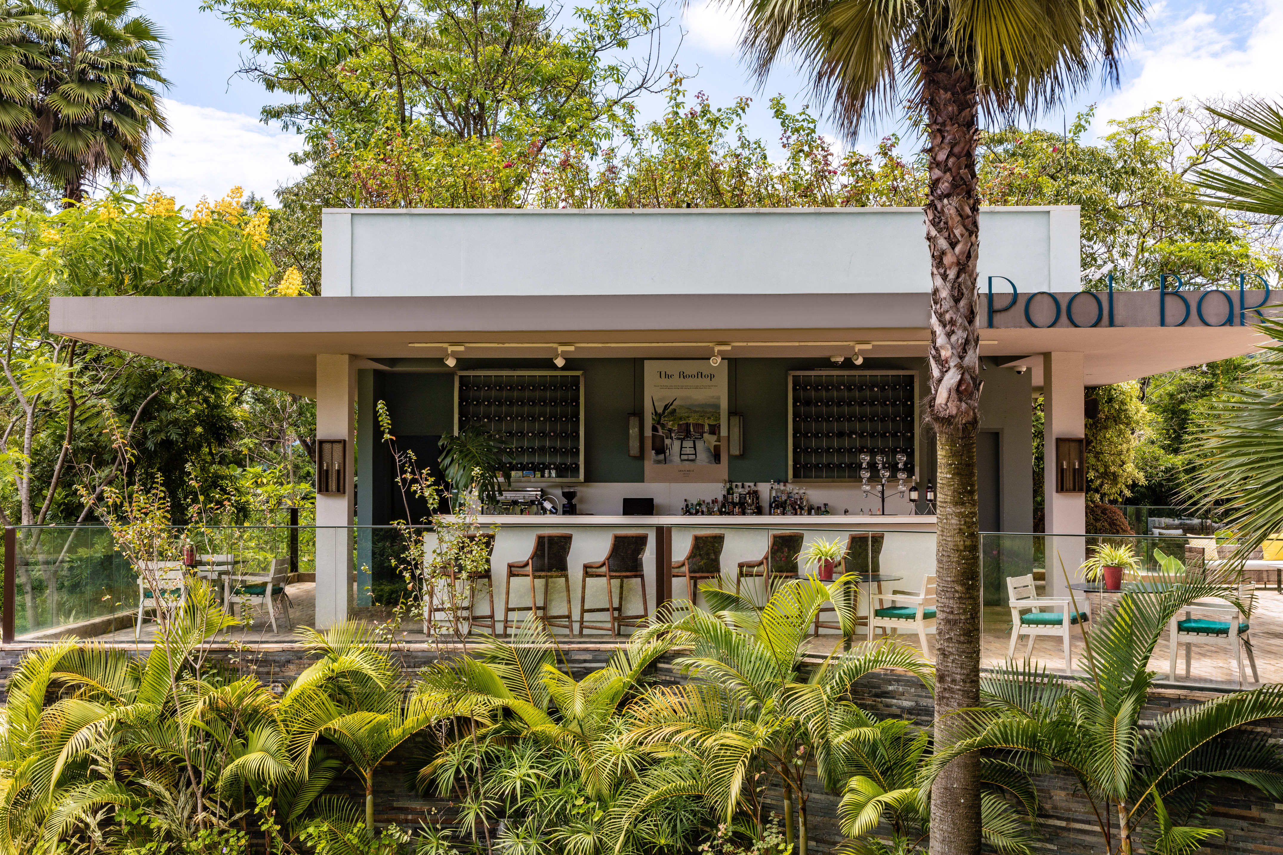 Pool bar at tropical resort with counter, stools, and lush palm trees.