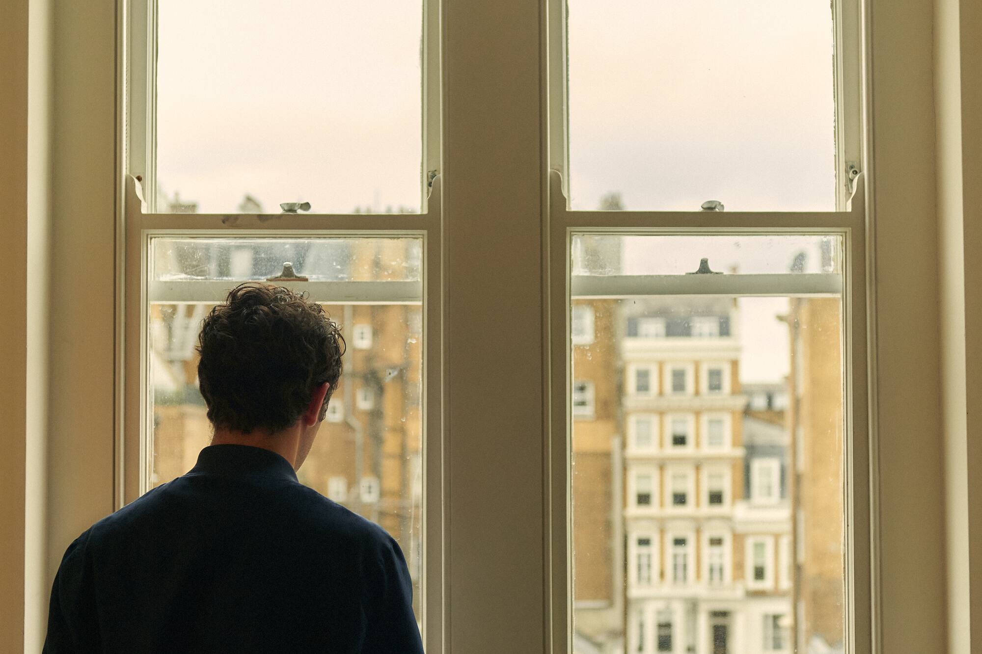 Hombre de espaldas mirando por ventana una vista de la ciudad.