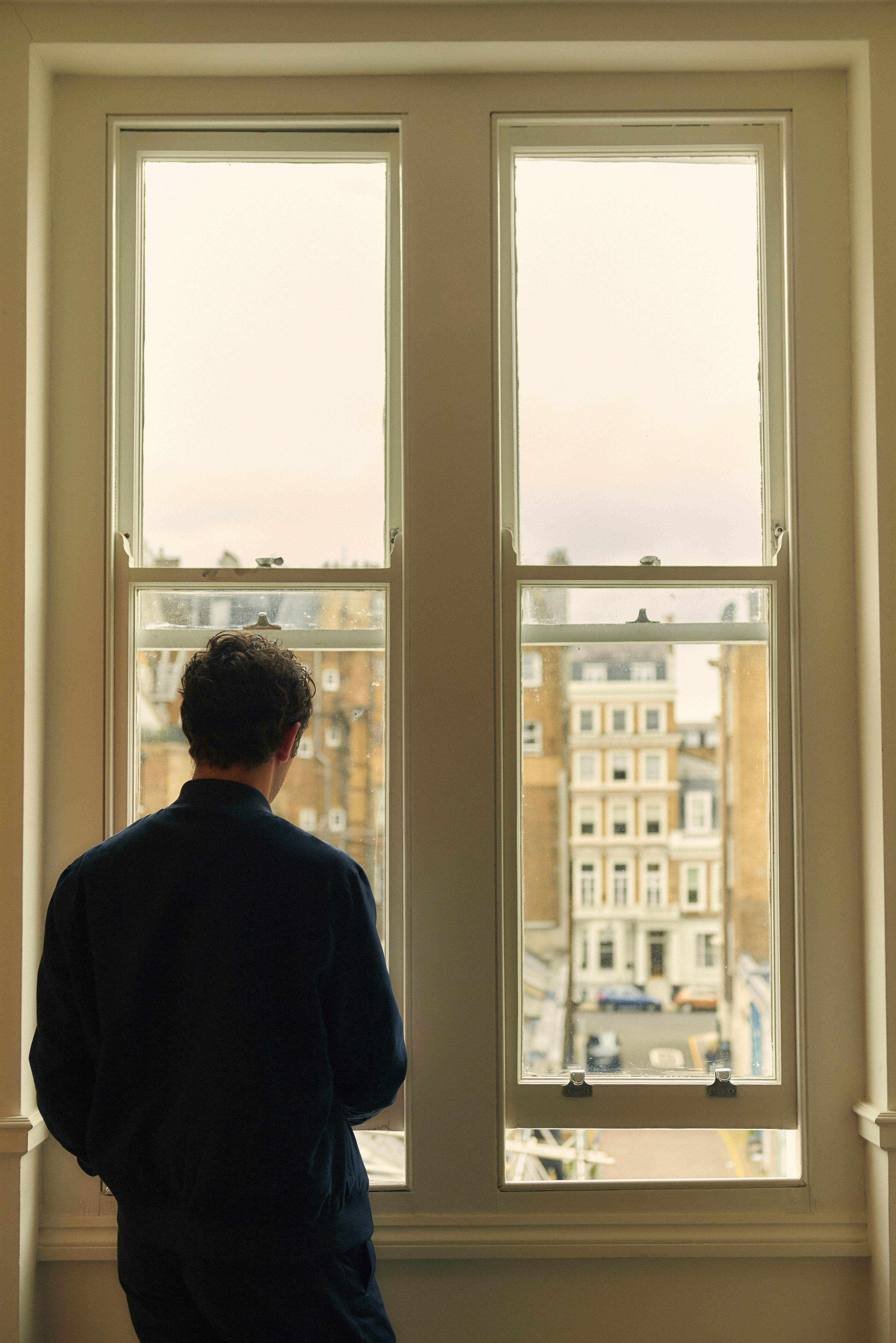 Hombre de espaldas mirando por ventana una vista de la ciudad.