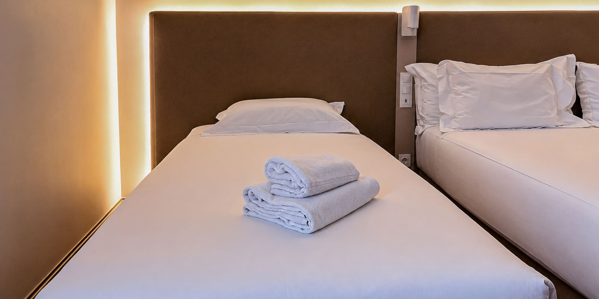 Twin hotel room with white beds, fresh towels, and warm ambient lighting.