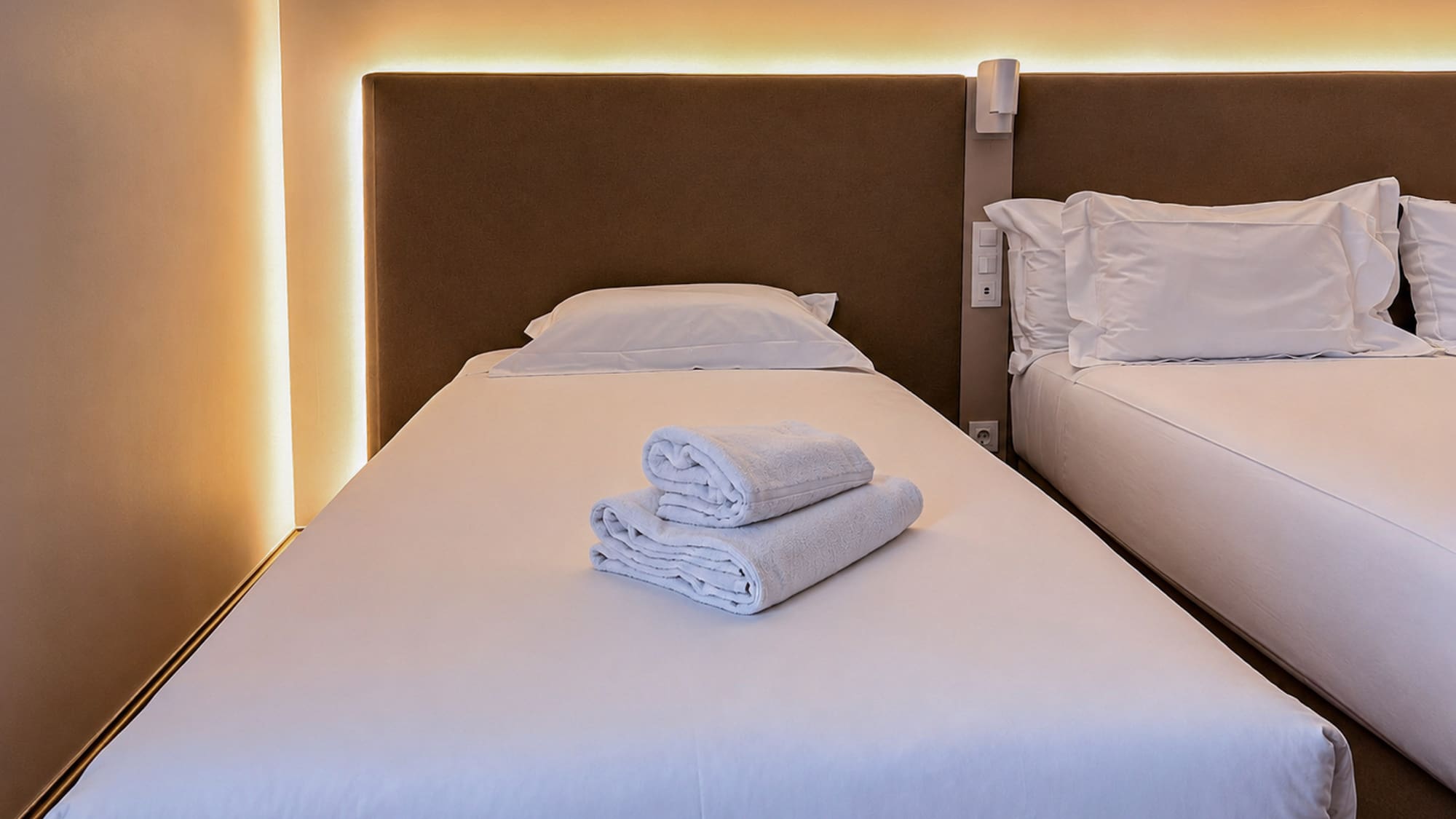Twin hotel room with white beds, fresh towels, and warm ambient lighting.