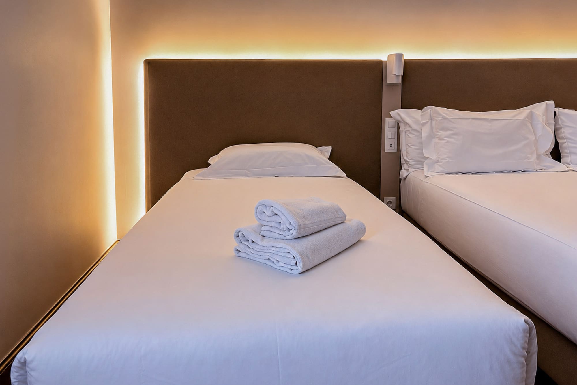 Twin hotel room with white beds, fresh towels, and warm ambient lighting.