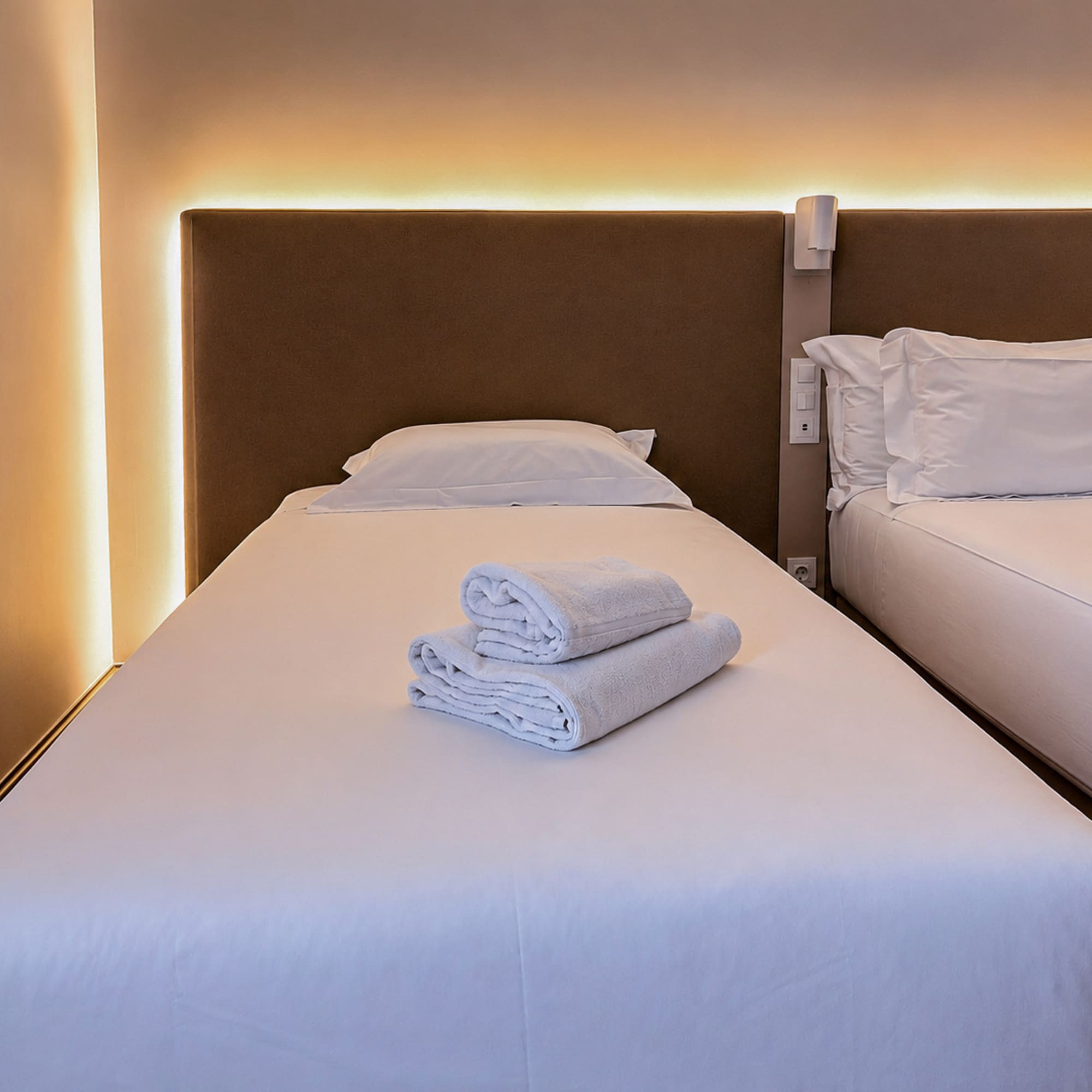 Twin hotel room with white beds, fresh towels, and warm ambient lighting.