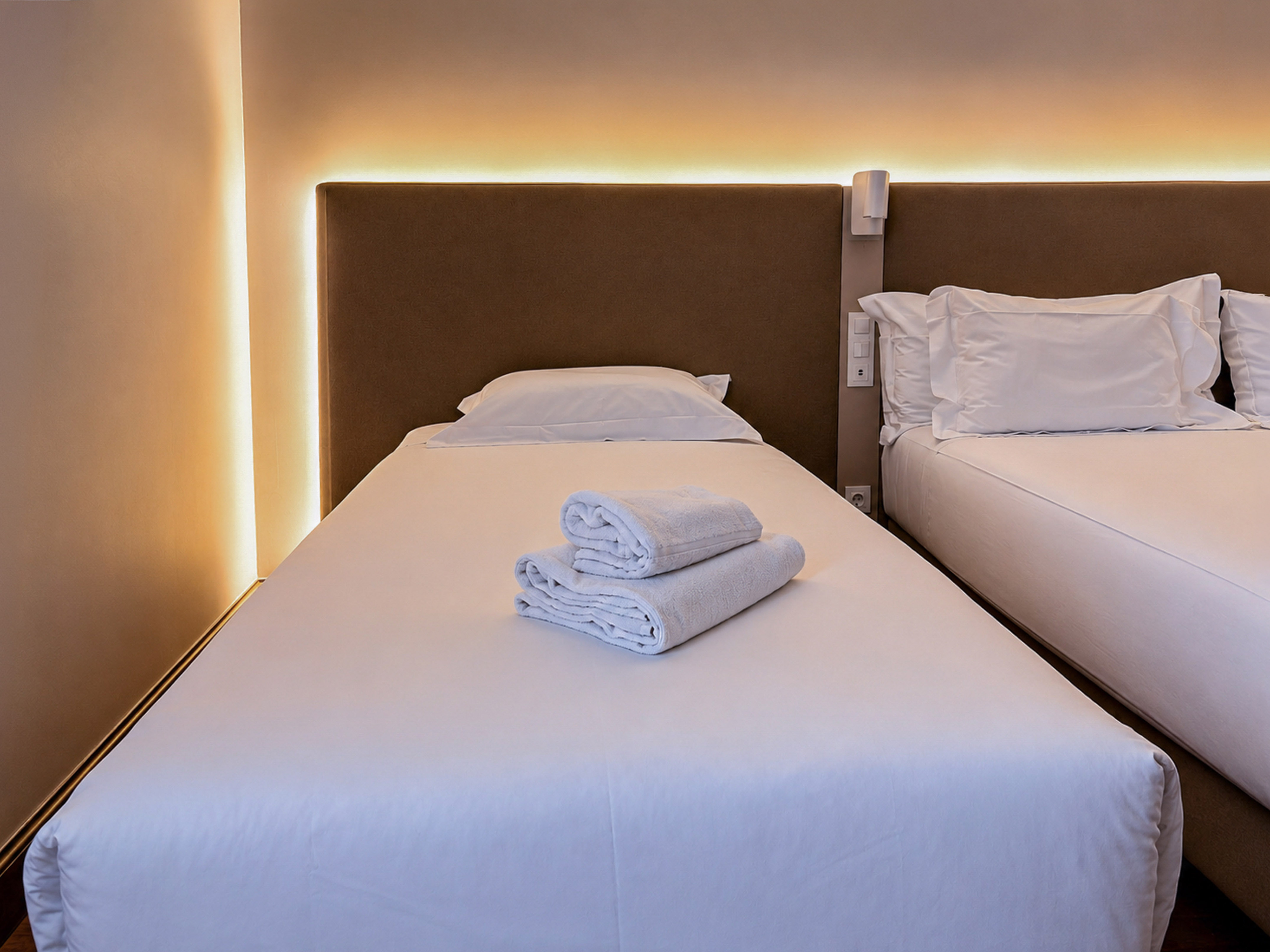 Twin hotel room with white beds, fresh towels, and warm ambient lighting.