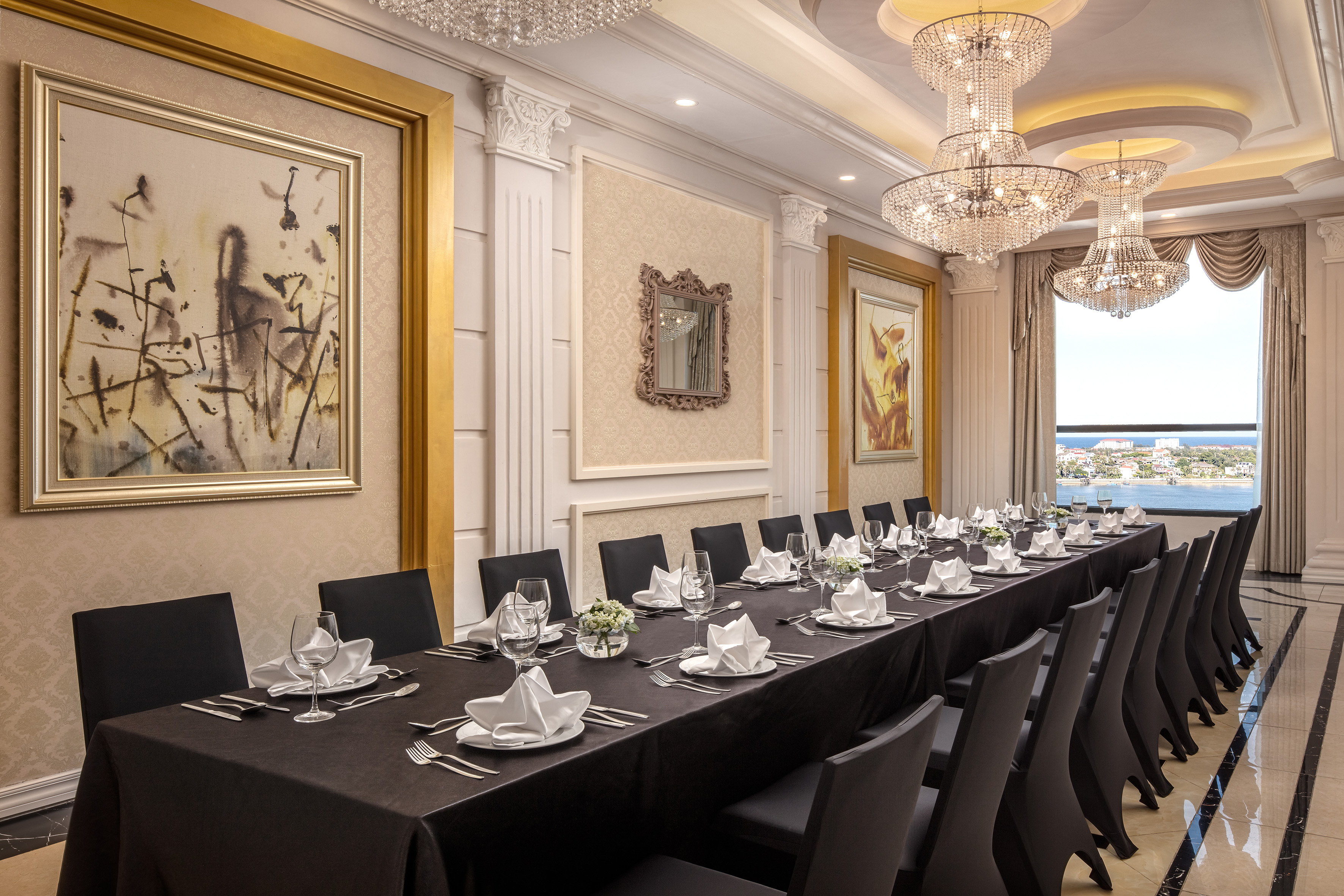 Luxurious formal dining room with long table, chandeliers, and ocean view.