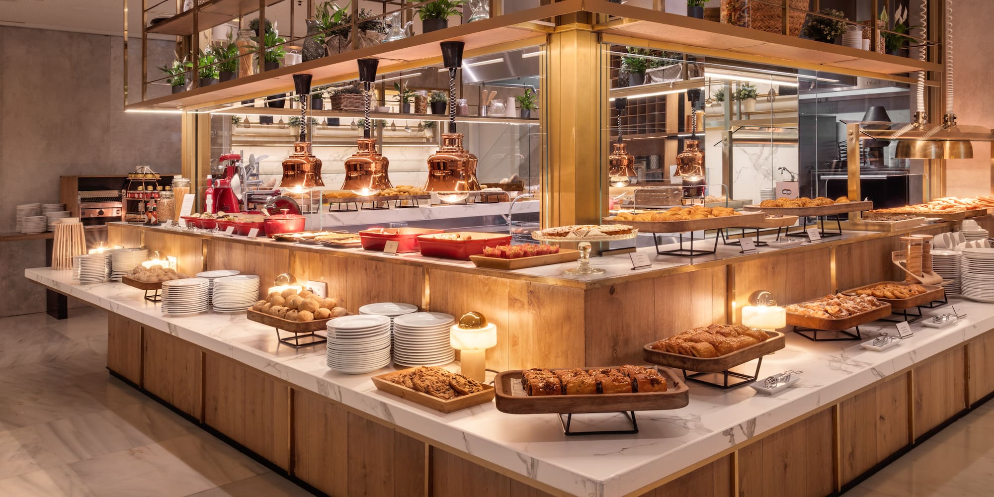 Modern hotel breakfast buffet with pastries, hot food, and warm lighting.