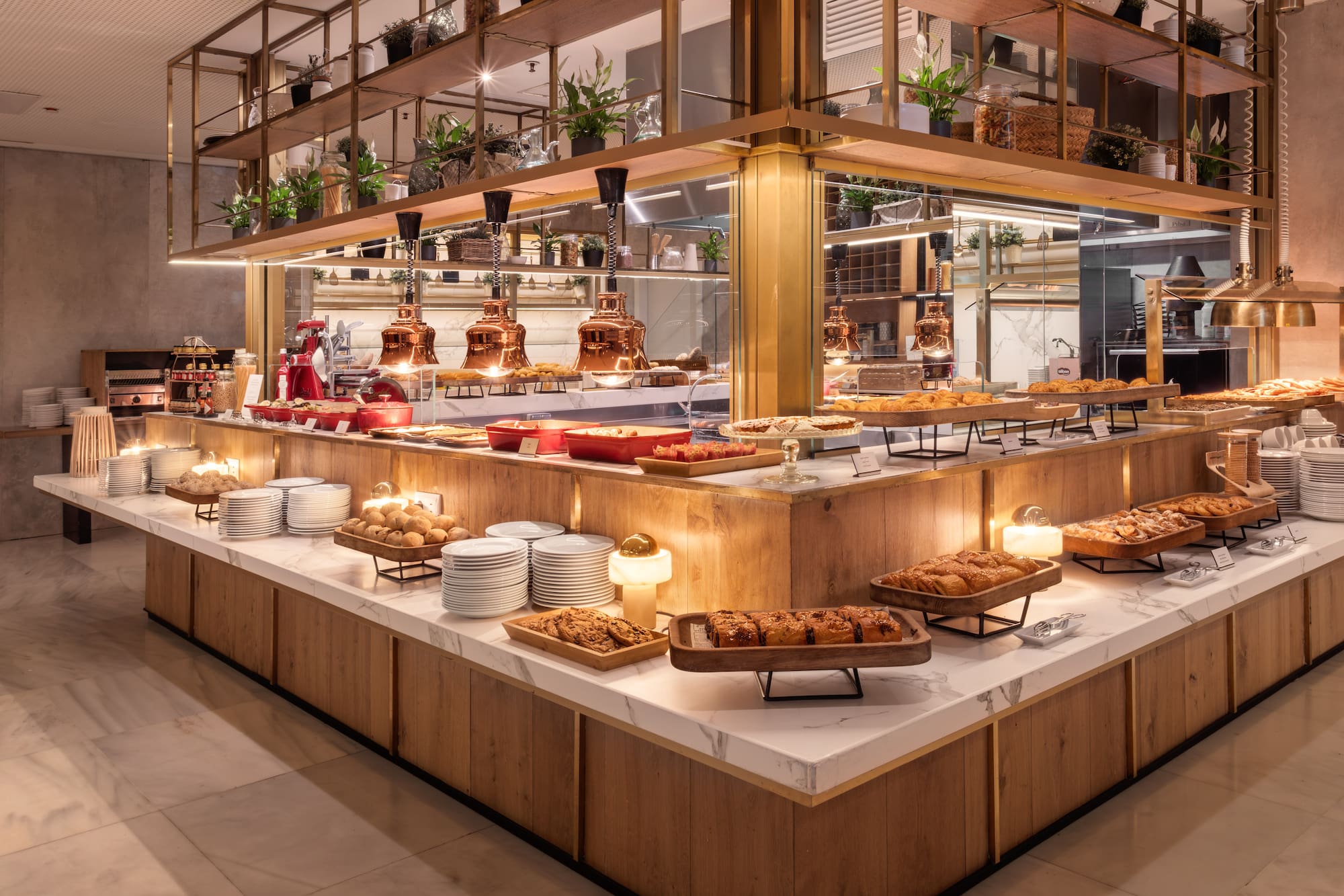 Modern hotel breakfast buffet with pastries, hot food, and warm lighting.
