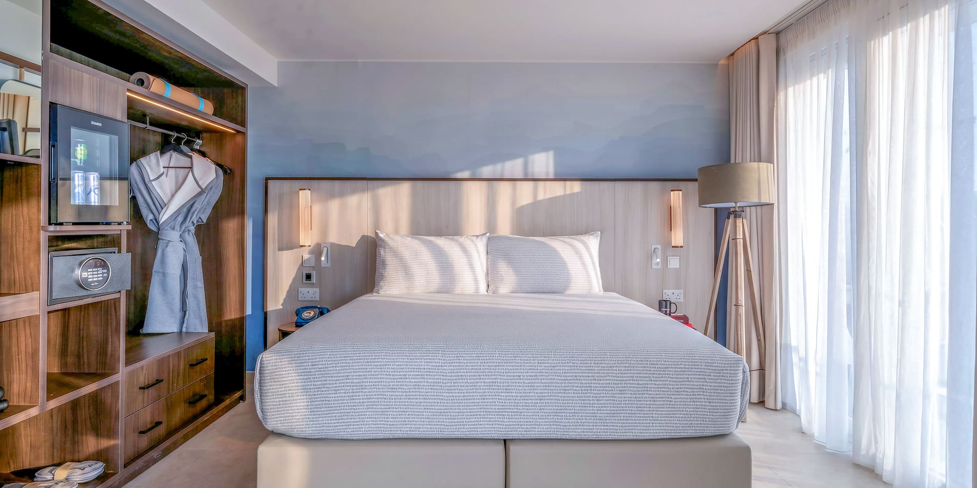 Bright, modern hotel bedroom with king bed, built-in storage, and sheer window curtains.