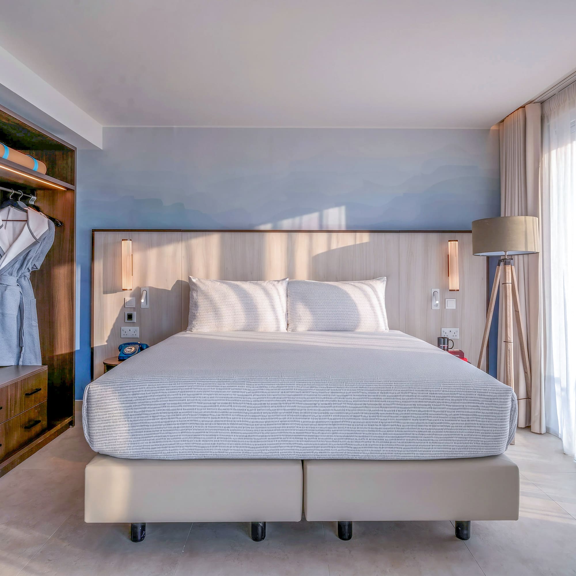 Bright, modern hotel bedroom with king bed, built-in storage, and sheer window curtains.