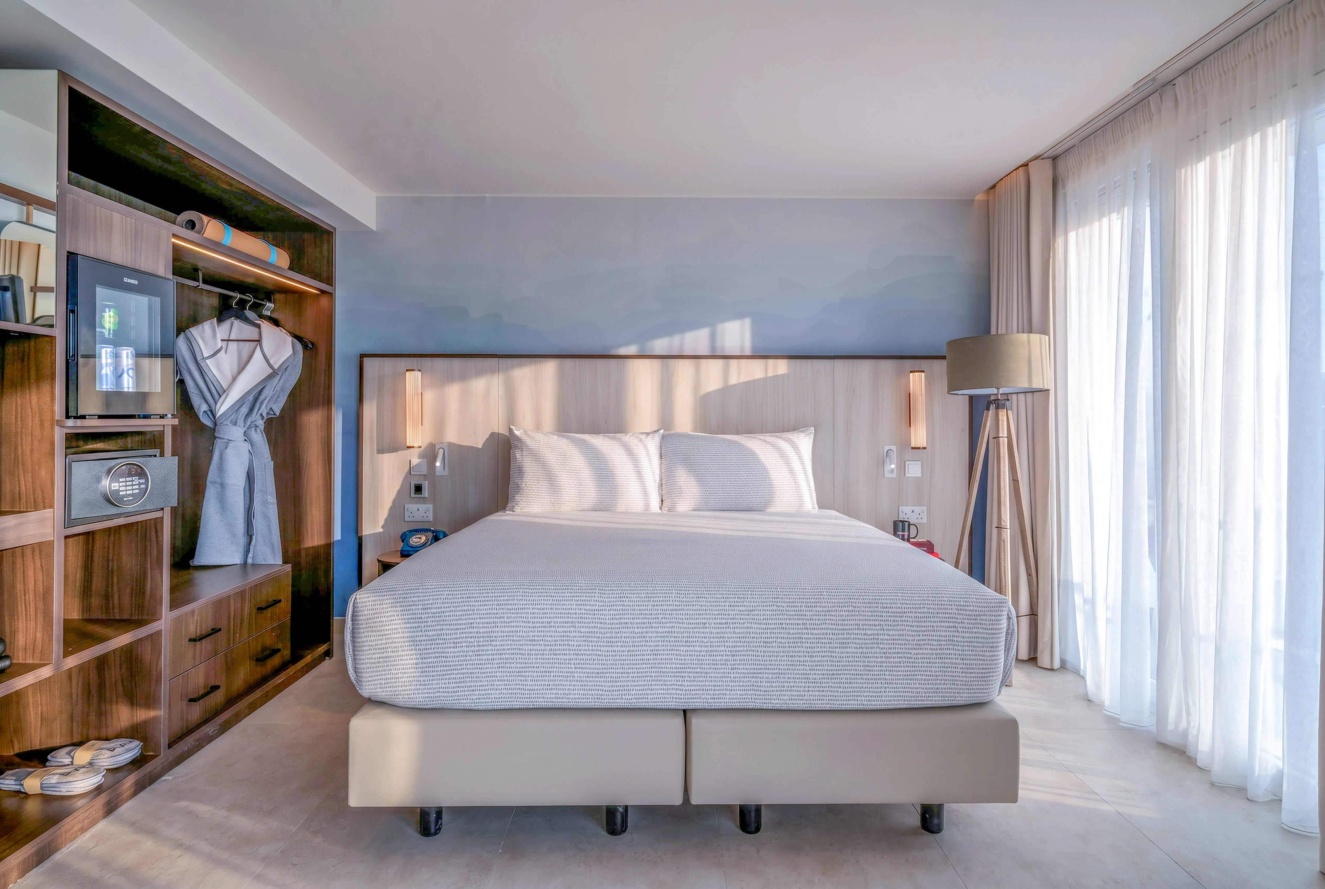 Bright, modern hotel bedroom with king bed, built-in storage, and sheer window curtains.