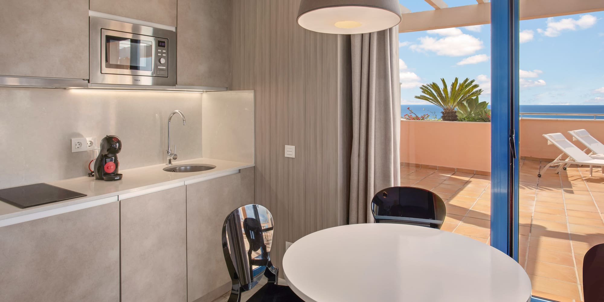 Modern kitchenette, dining area, and balcony with ocean view.
