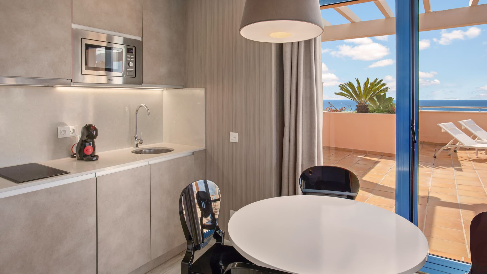 Modern kitchenette, dining area, and balcony with ocean view.