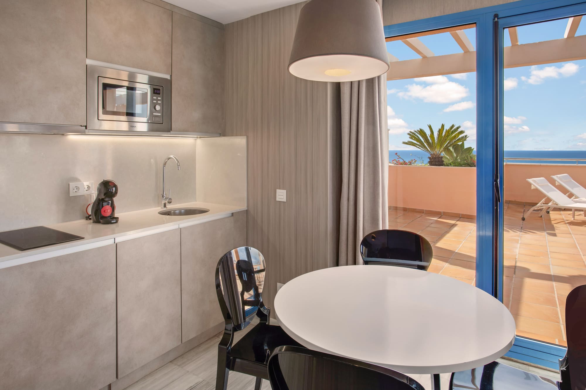 Modern kitchenette, dining area, and balcony with ocean view.