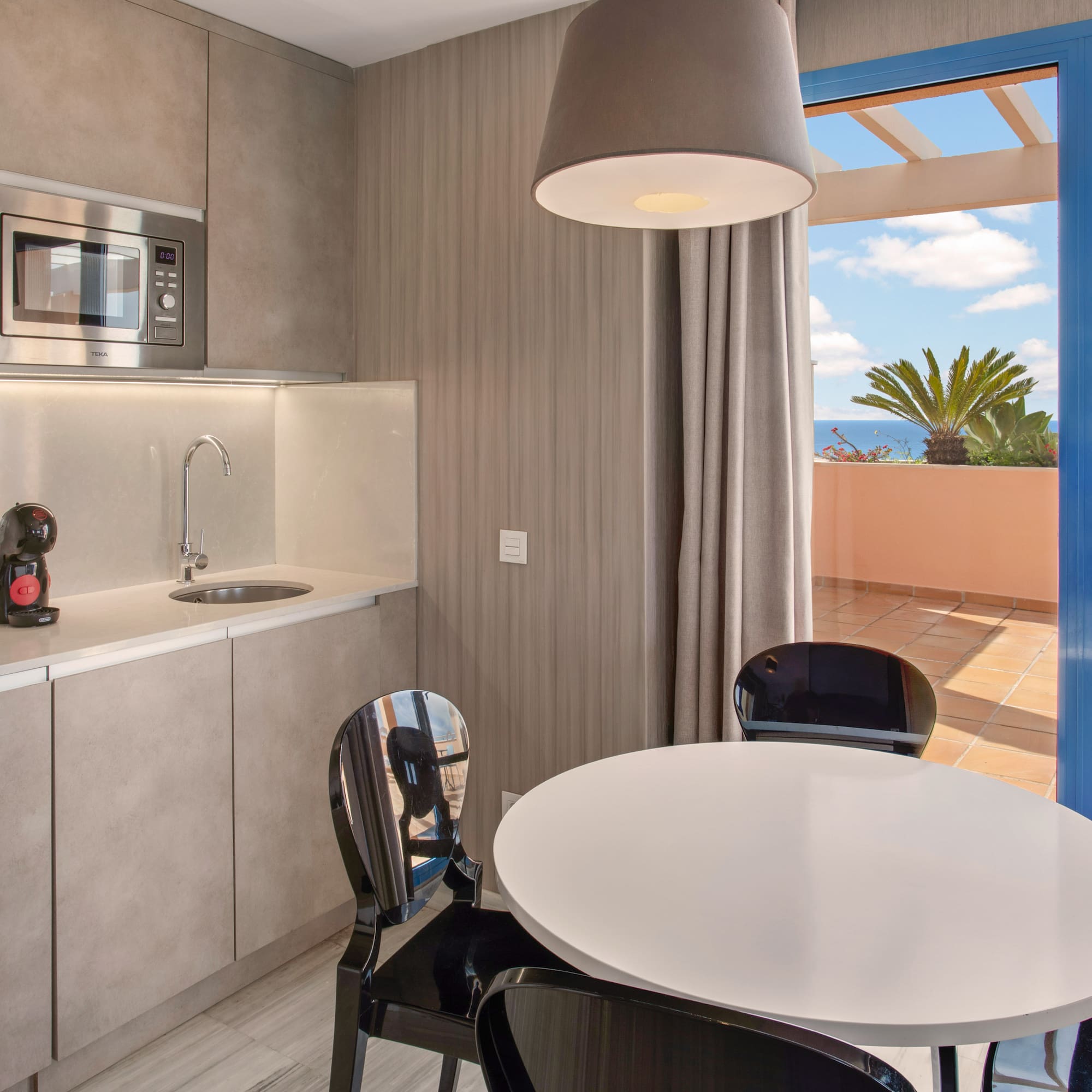 Modern kitchenette, dining area, and balcony with ocean view.