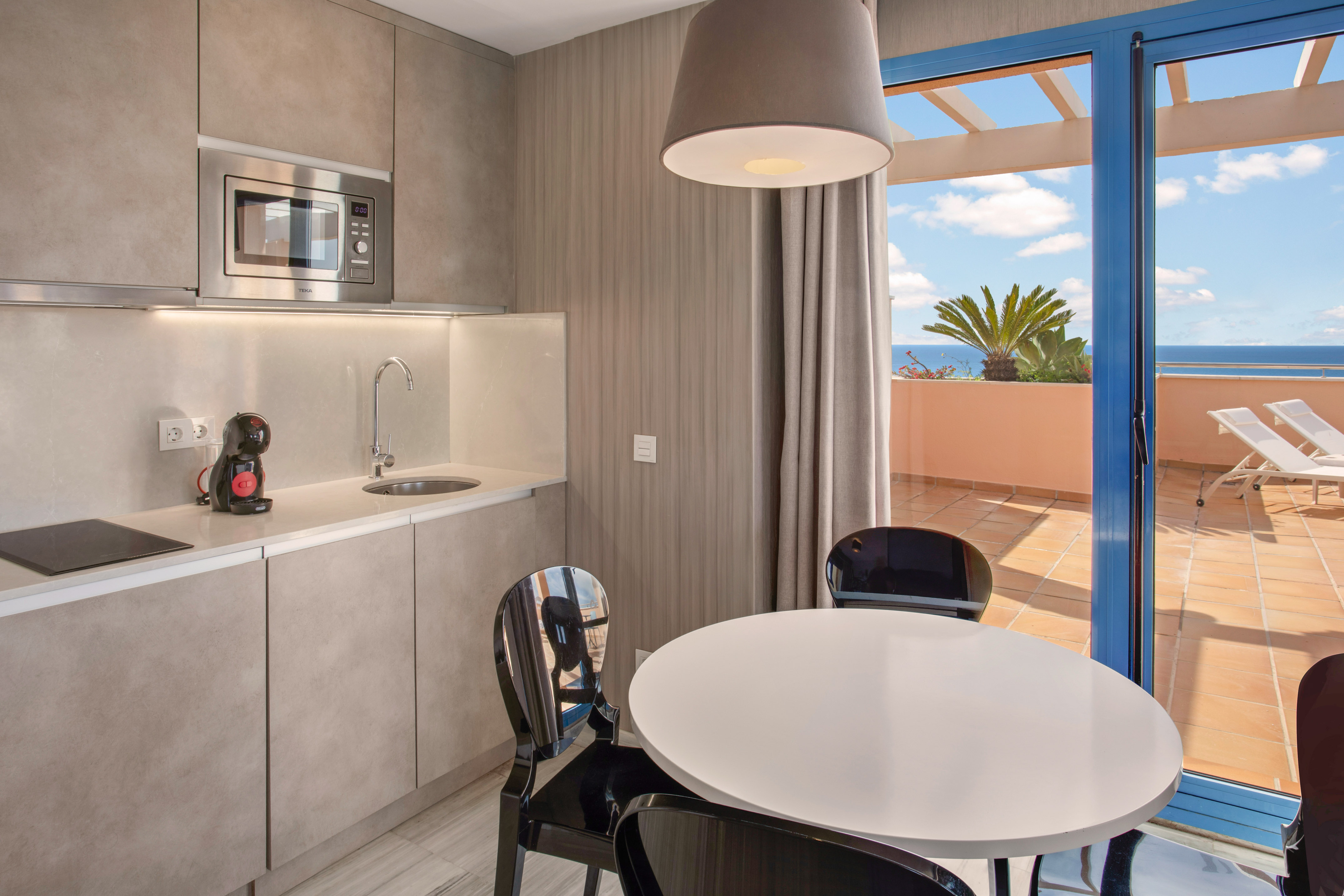 Modern kitchenette, dining area, and balcony with ocean view.
