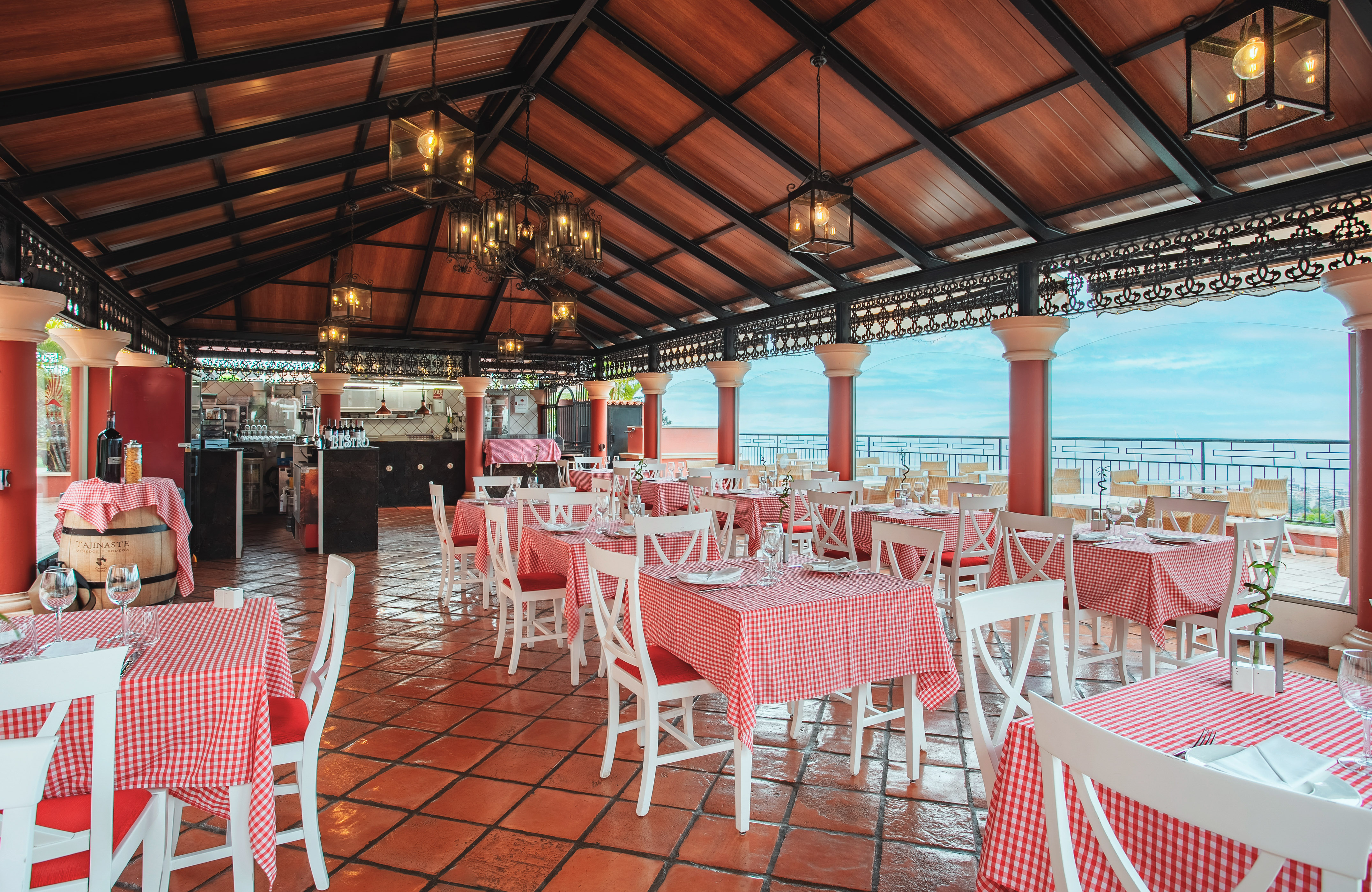 Outdoor restaurant dining area with red checkered tables and ocean view.