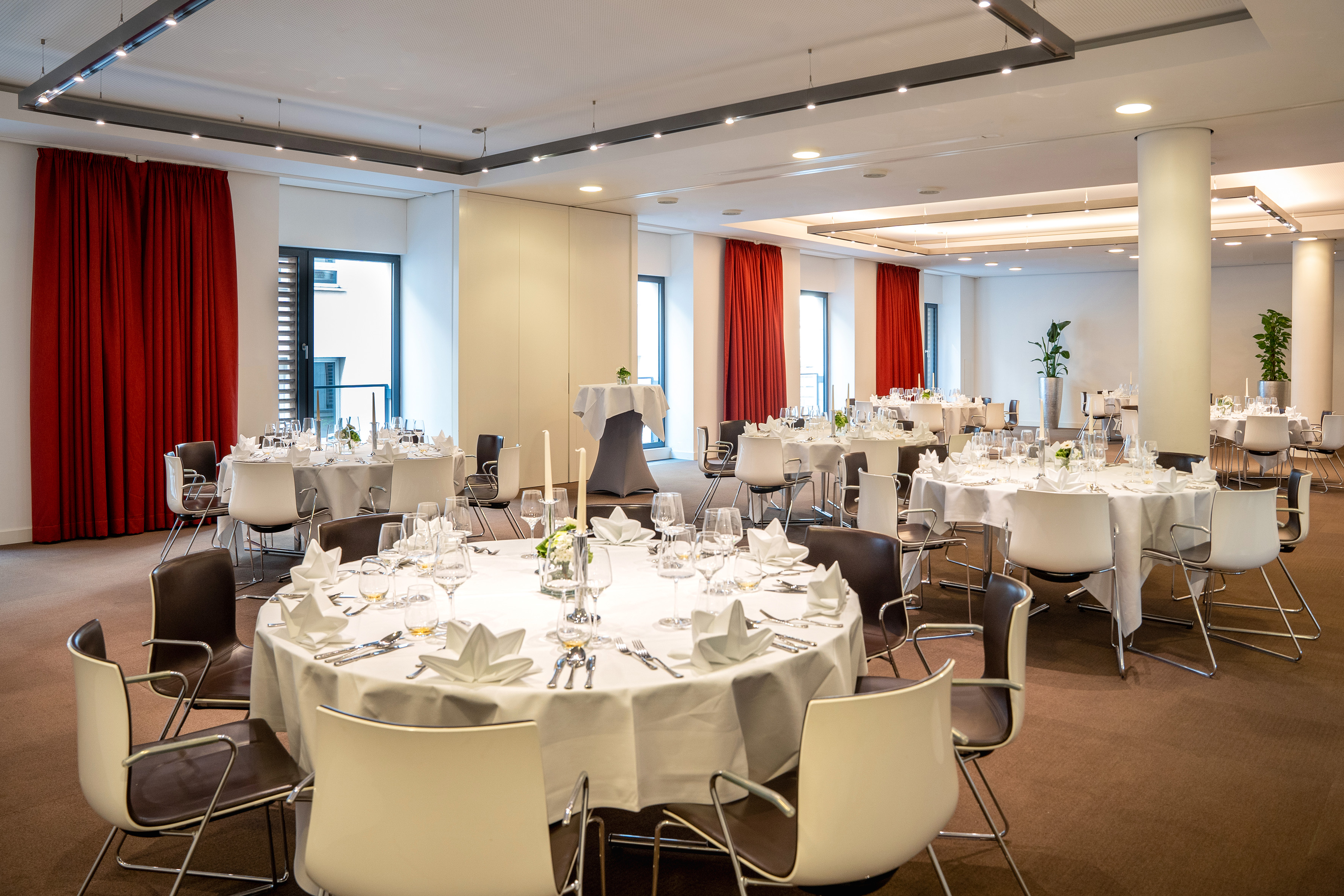 Modern banquet hall with round tables, white linens, and red drapes. - CONEins + Zwei + Drei - Innside Dresda, Dresda