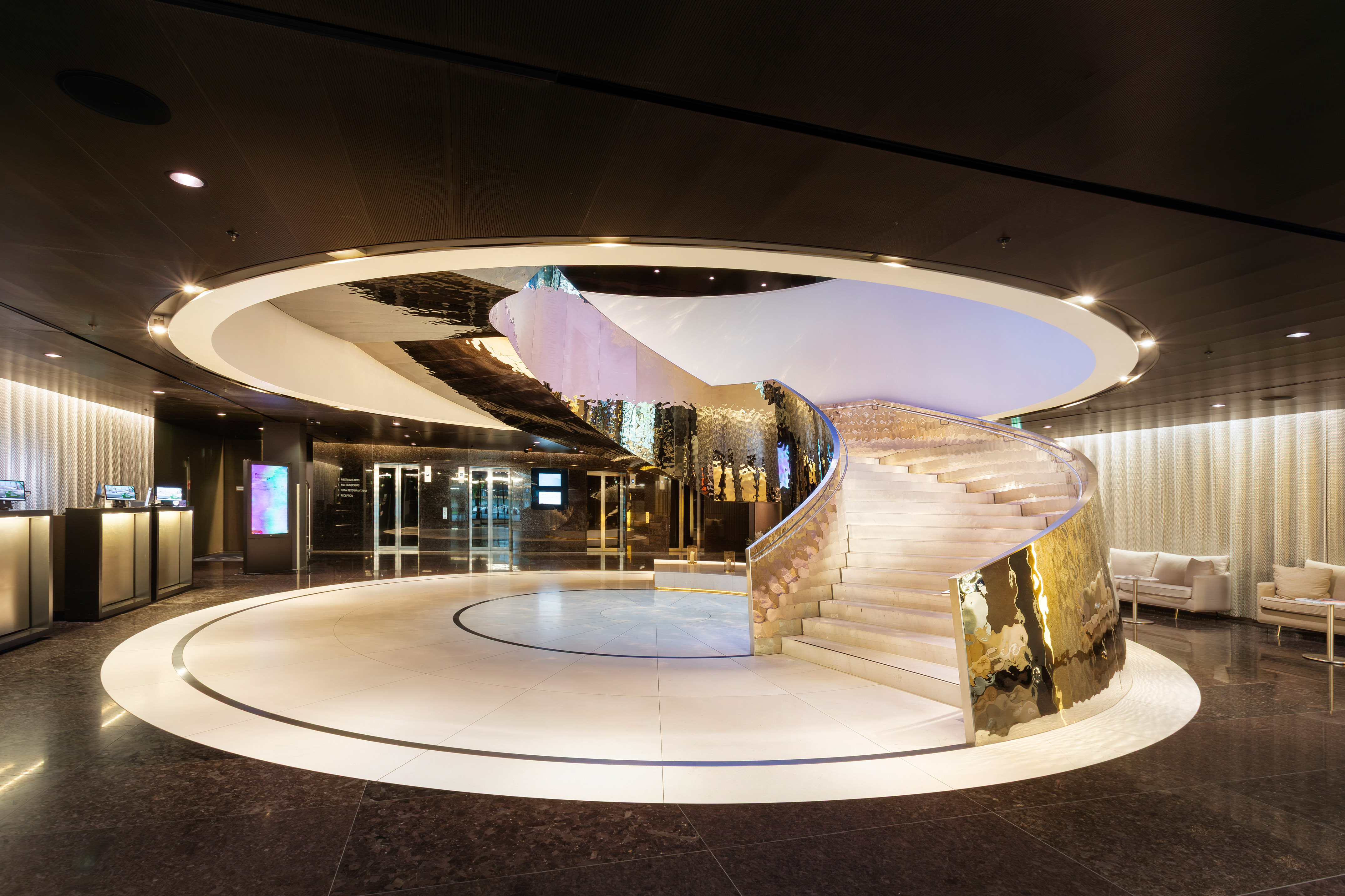 Luxury hotel lobby with white spiral staircase, gold accents, and circular floor.