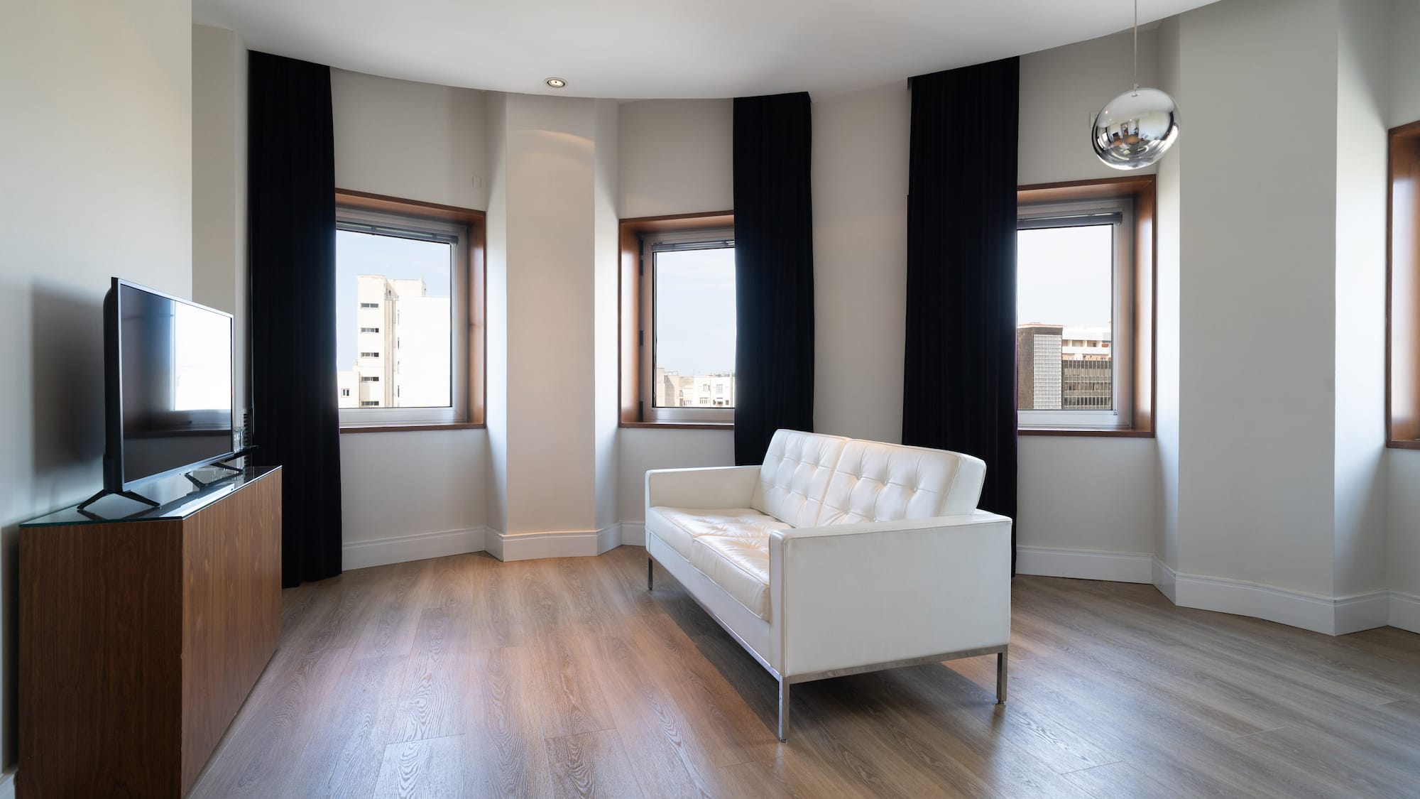 Contemporary living room with white sofa, wood floor, TV, and curved windows.