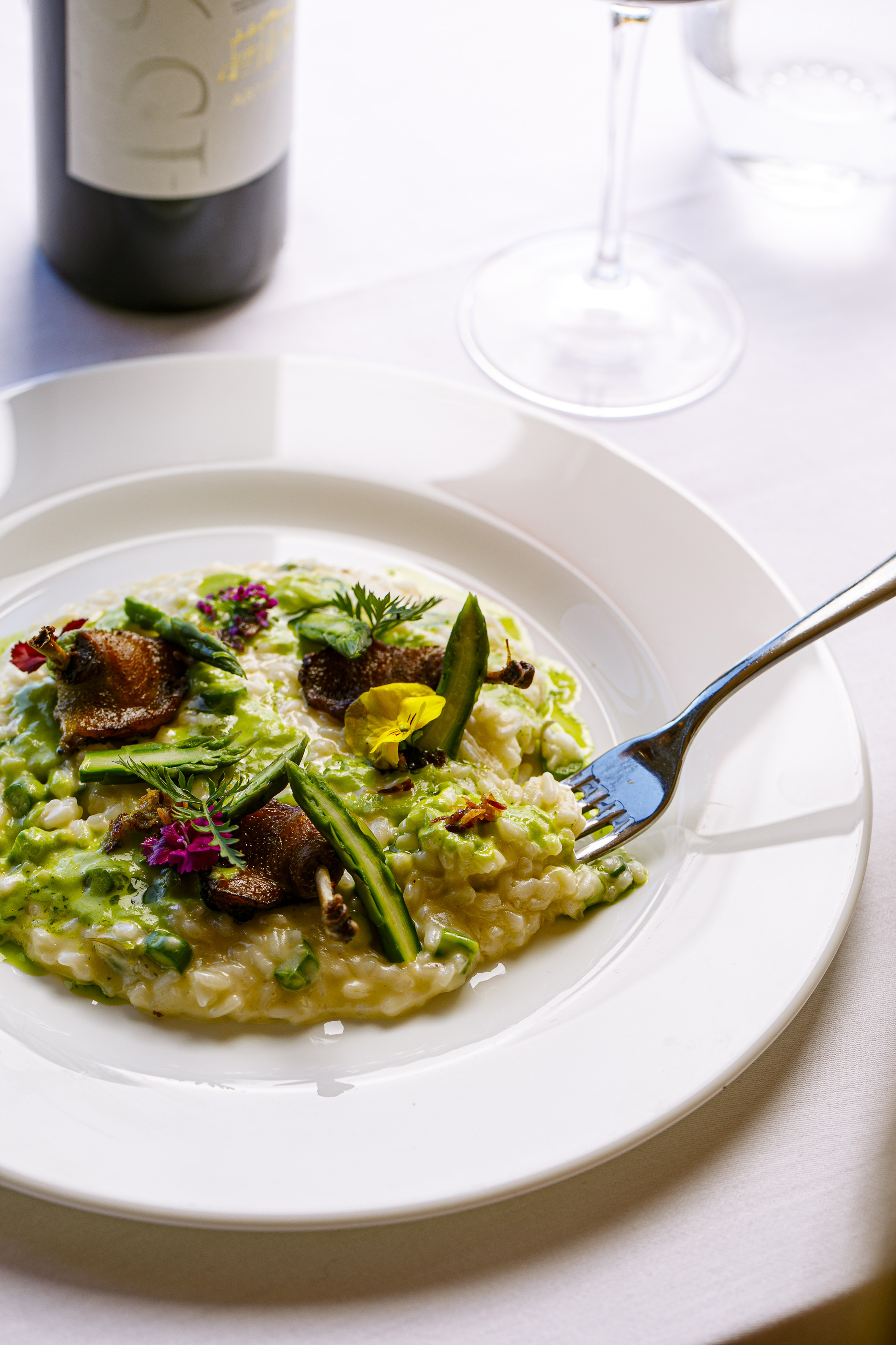 Creamy duck and asparagus risotto with peas, topped with herbs, fork in dish.
