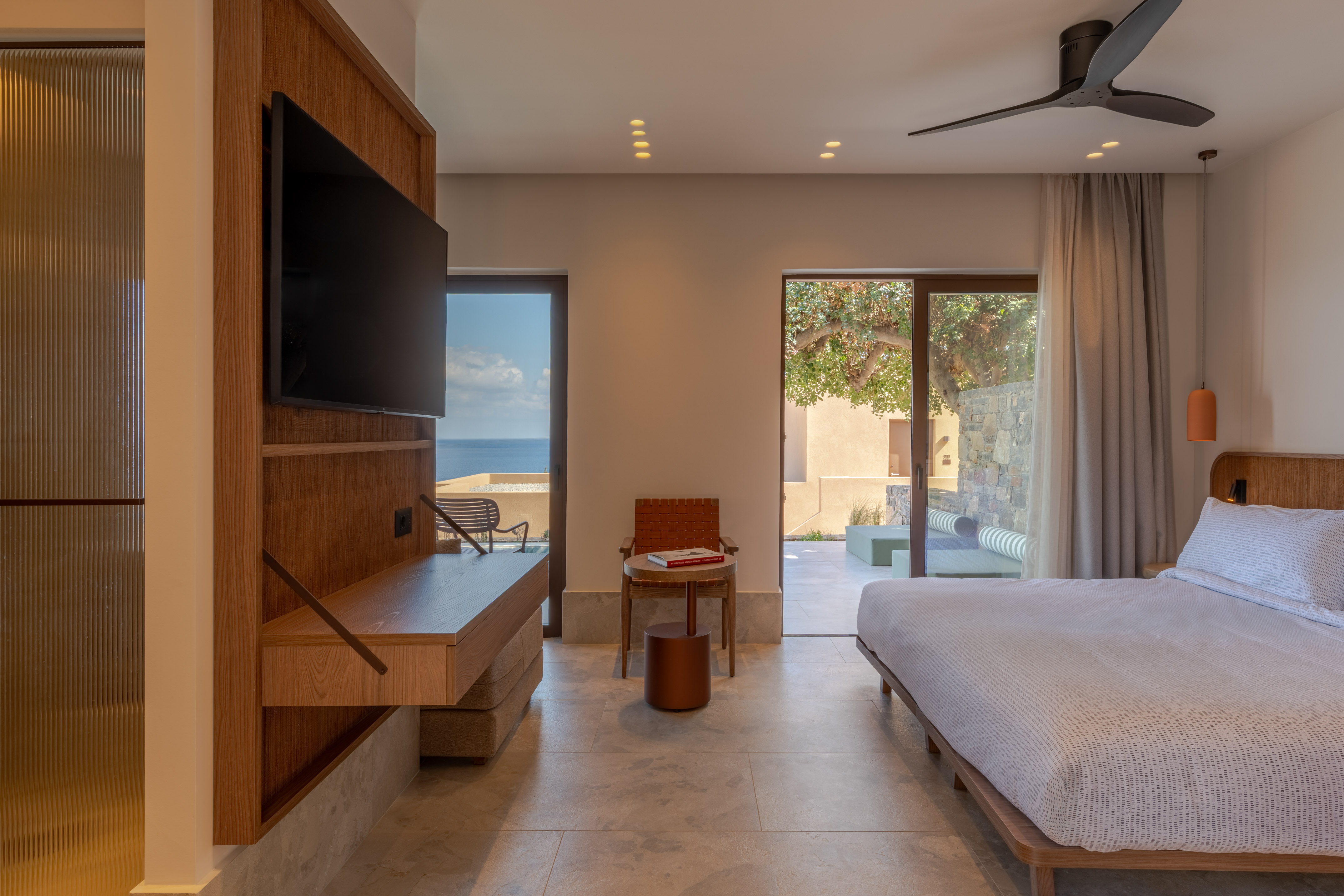 Modern hotel bedroom with ocean view, large bed, TV, and private terrace access.