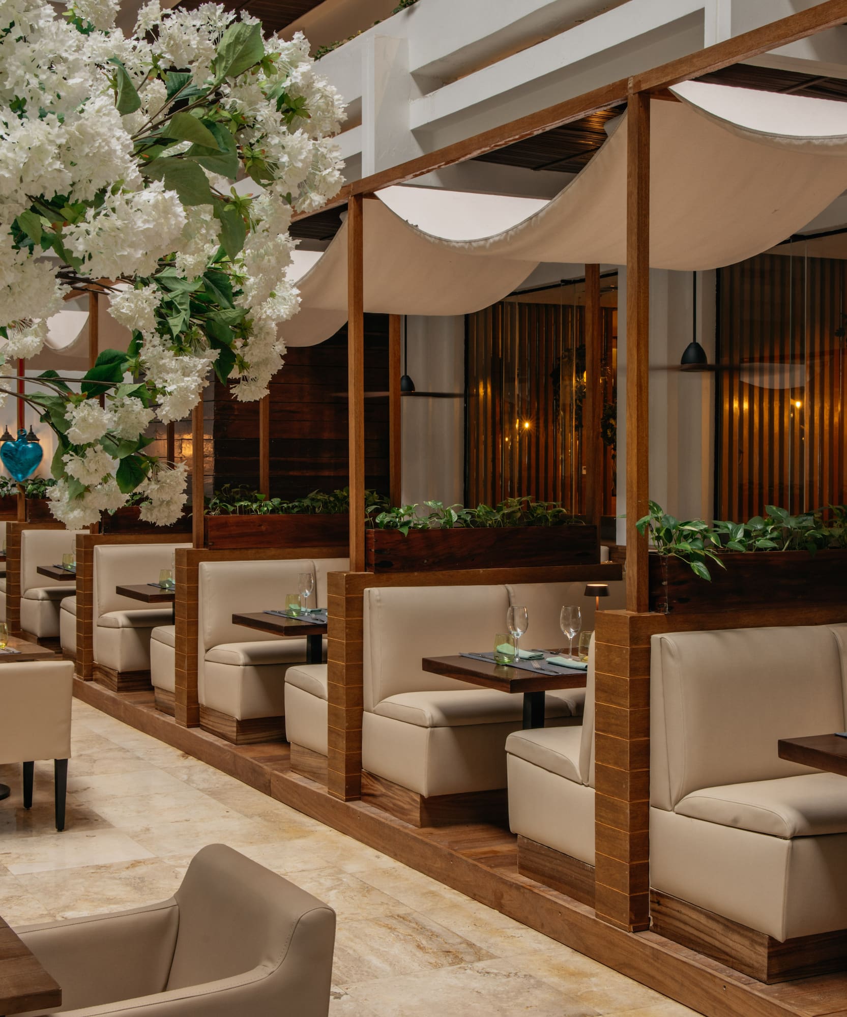 Elegant restaurant interior with white blossoms, beige booths, and canopy dining.