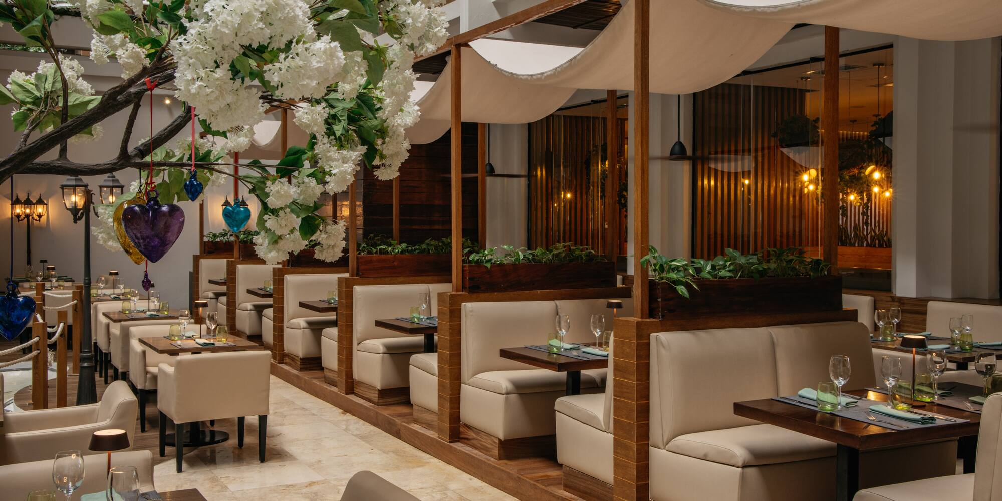 Elegant restaurant interior with white blossoms, beige booths, and canopy dining.
