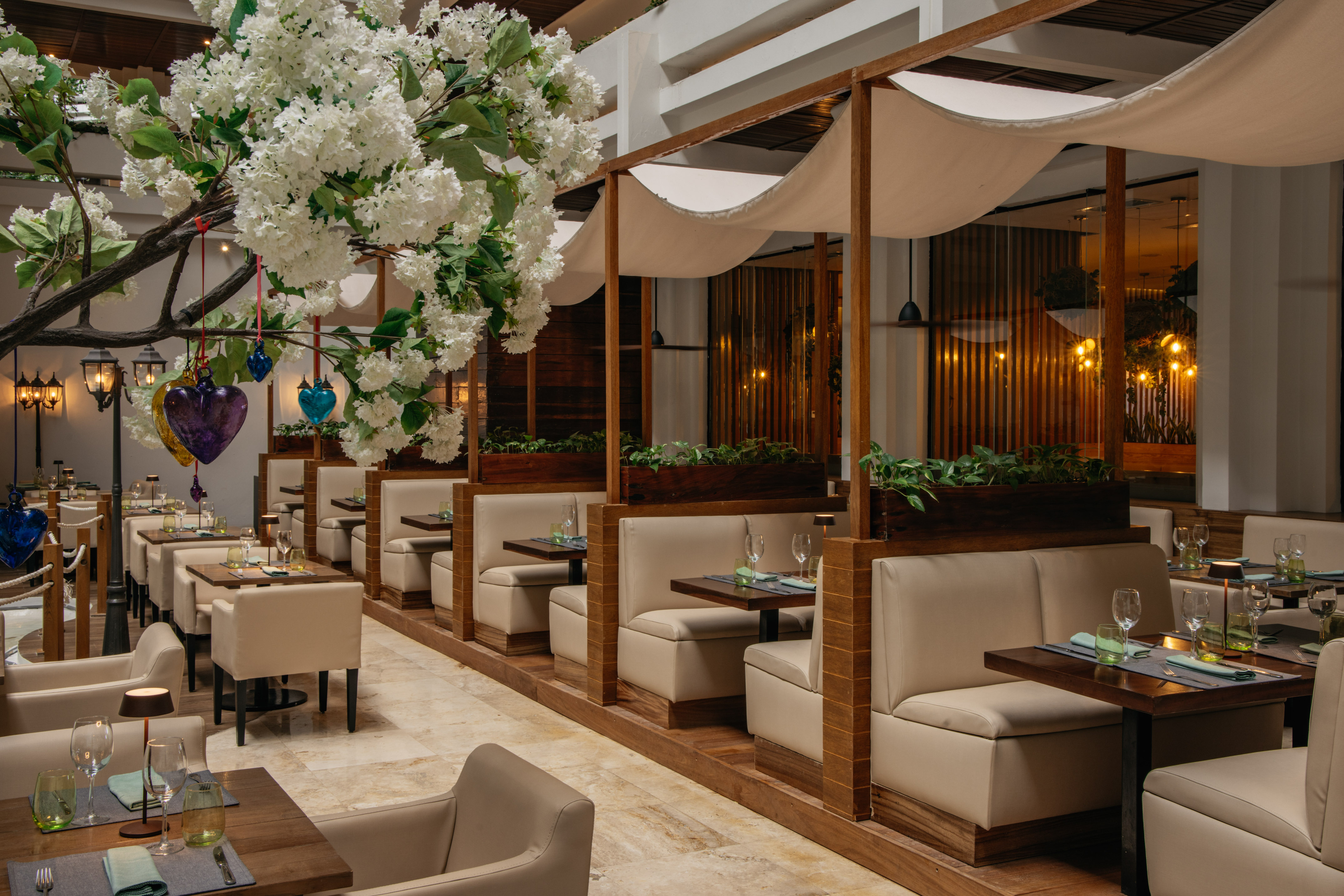 Elegant restaurant interior with white blossoms, beige booths, and canopy dining.