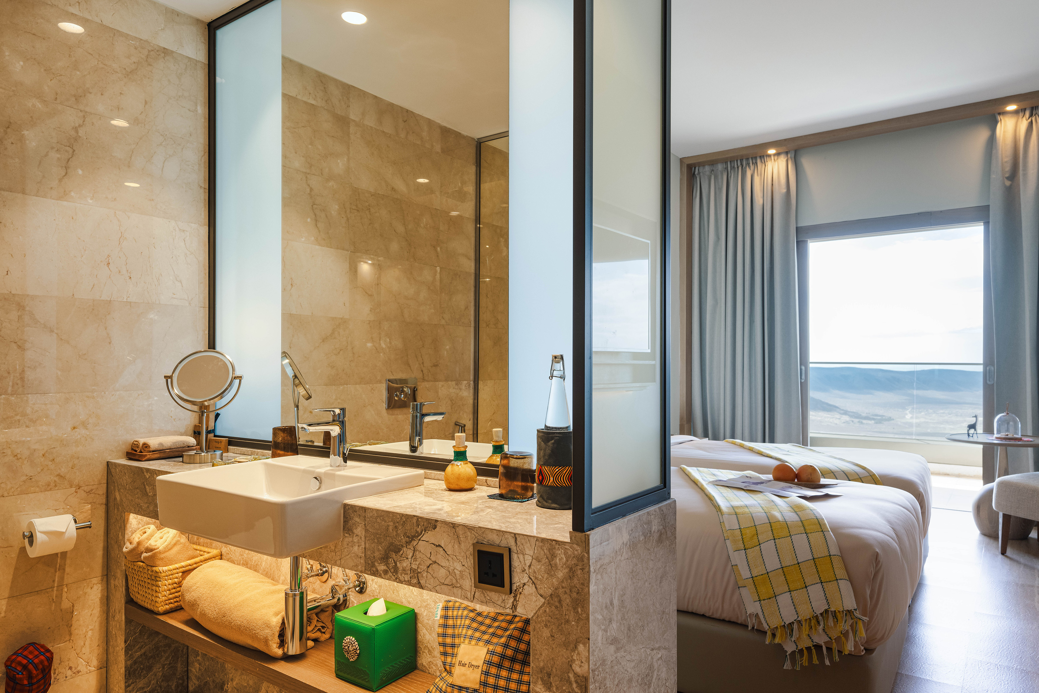 Luxury hotel suite with modern bathroom vanity, beds, and scenic landscape view.
