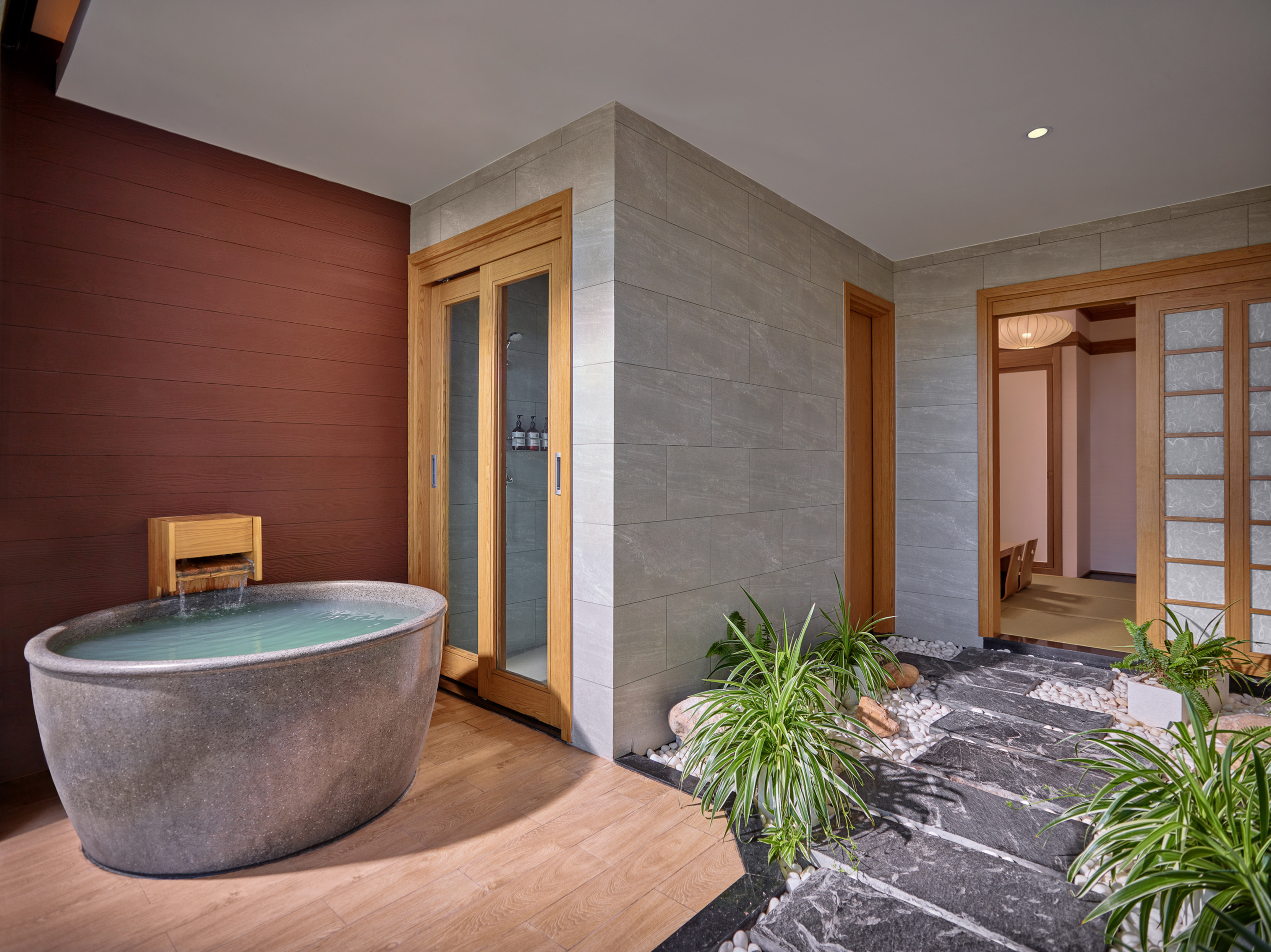Japanese-style bathroom with stone soaking tub, wooden floor, and zen garden.