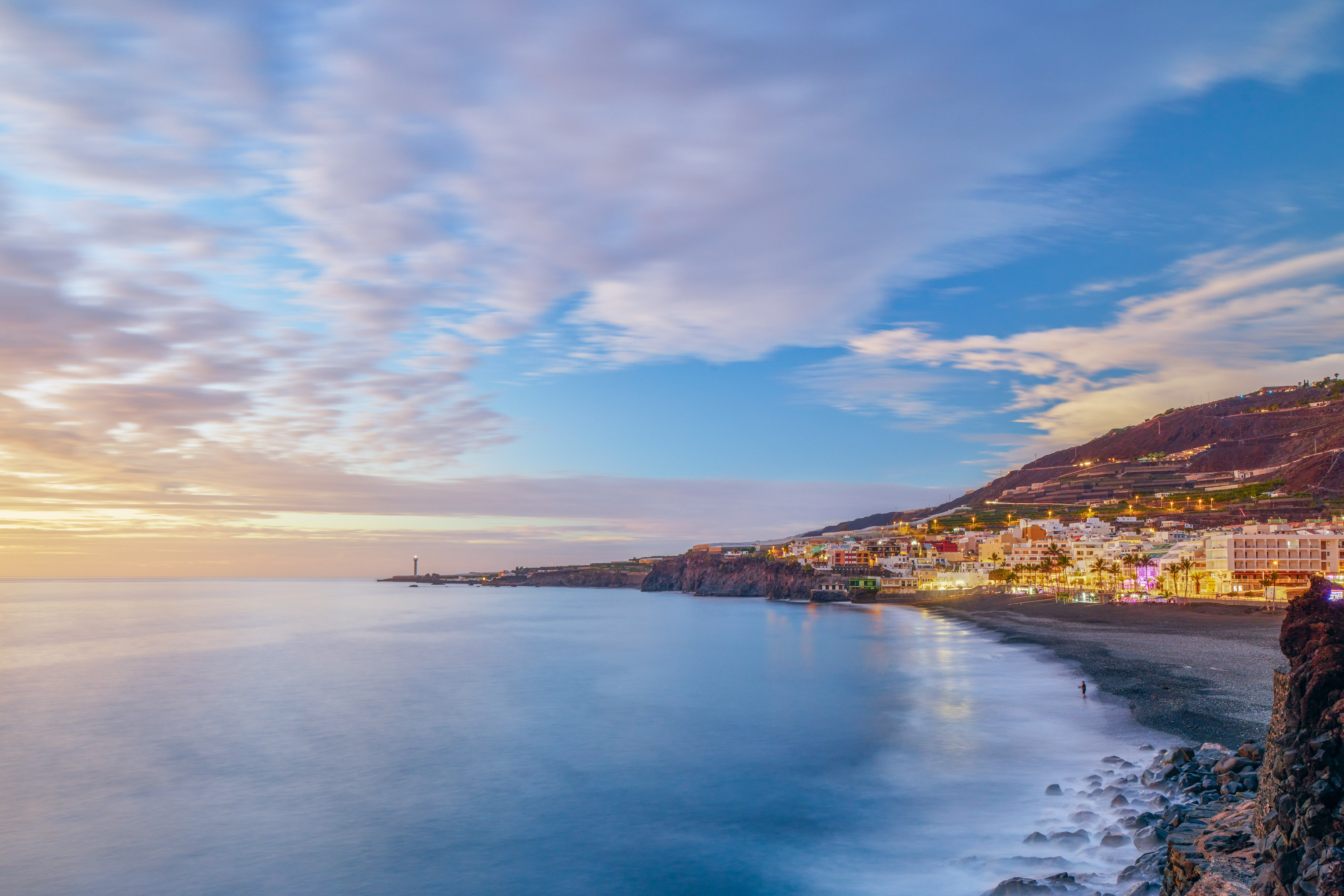 Coastal town at twilight, lighthouse, smooth ocean, illuminated buildings.