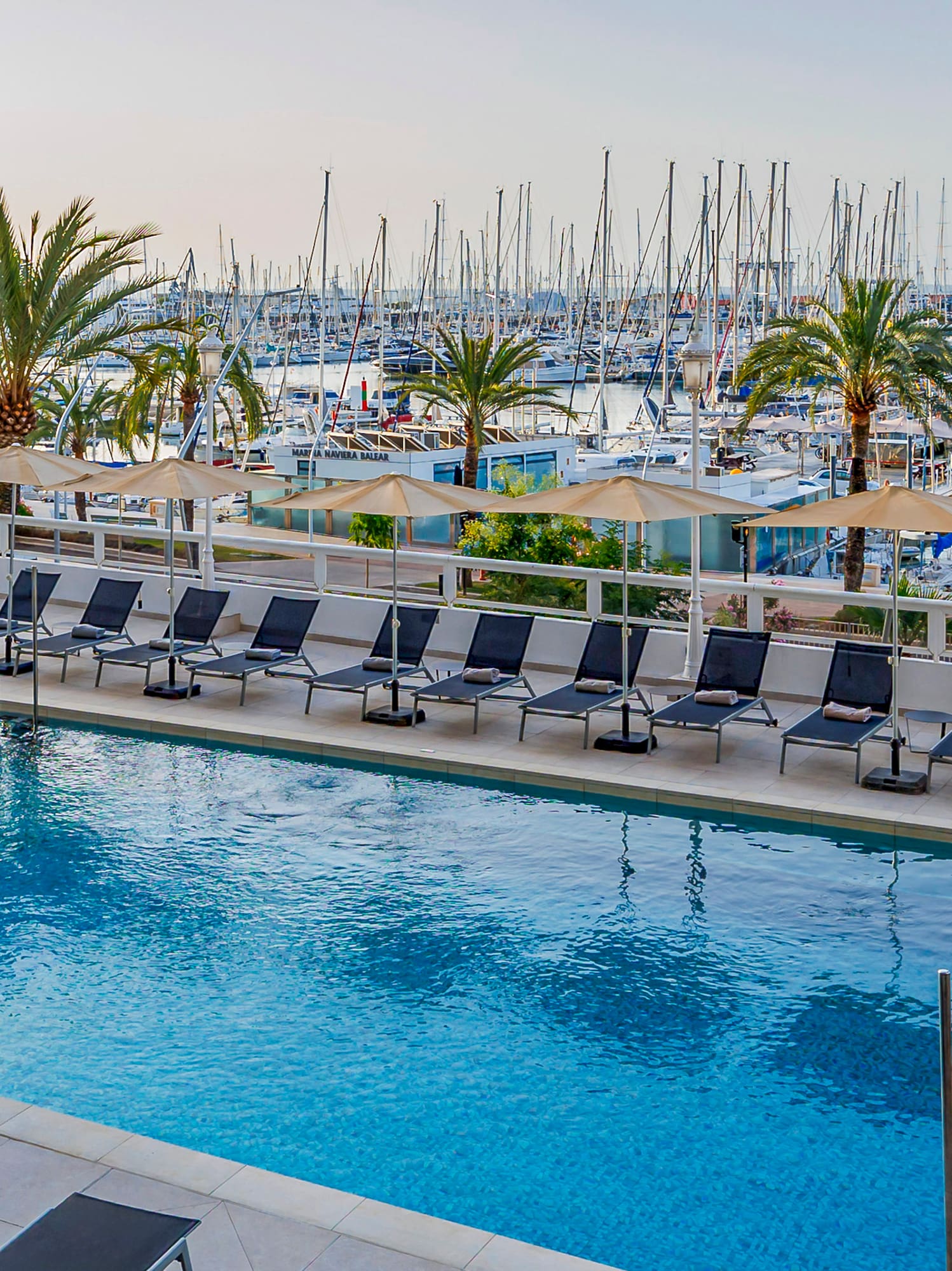 Piscina de hotel frente a puerto deportivo con barcos y la Catedral de Palma.
