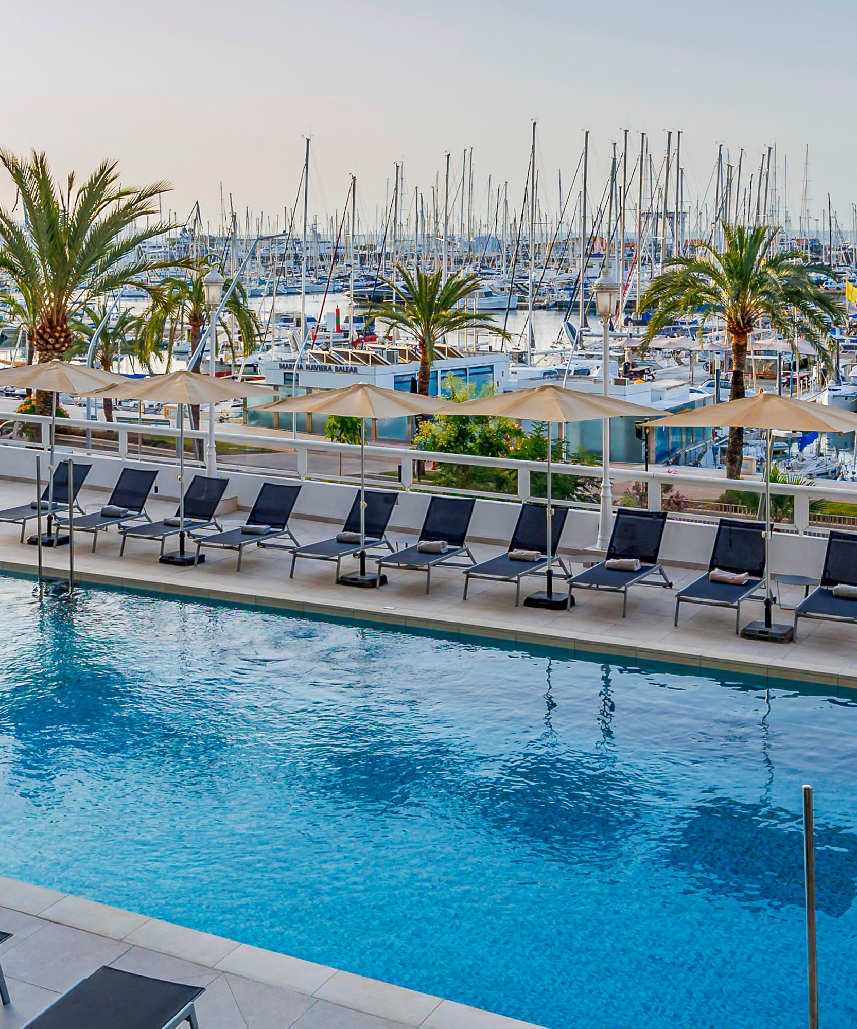 Piscina de hotel frente a puerto deportivo con barcos y la Catedral de Palma.