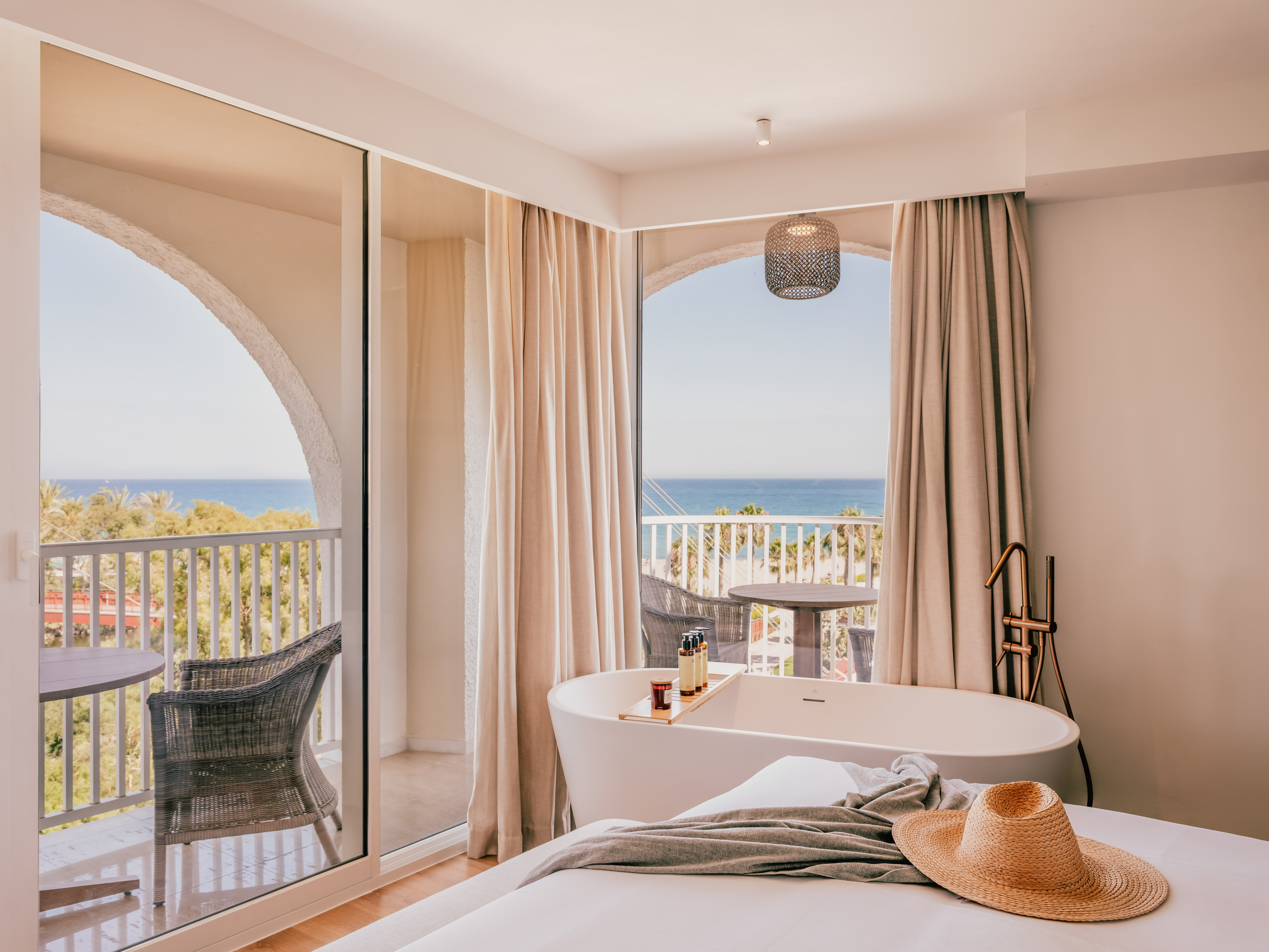 Luxury hotel suite with ocean view, freestanding bathtub, and balcony.