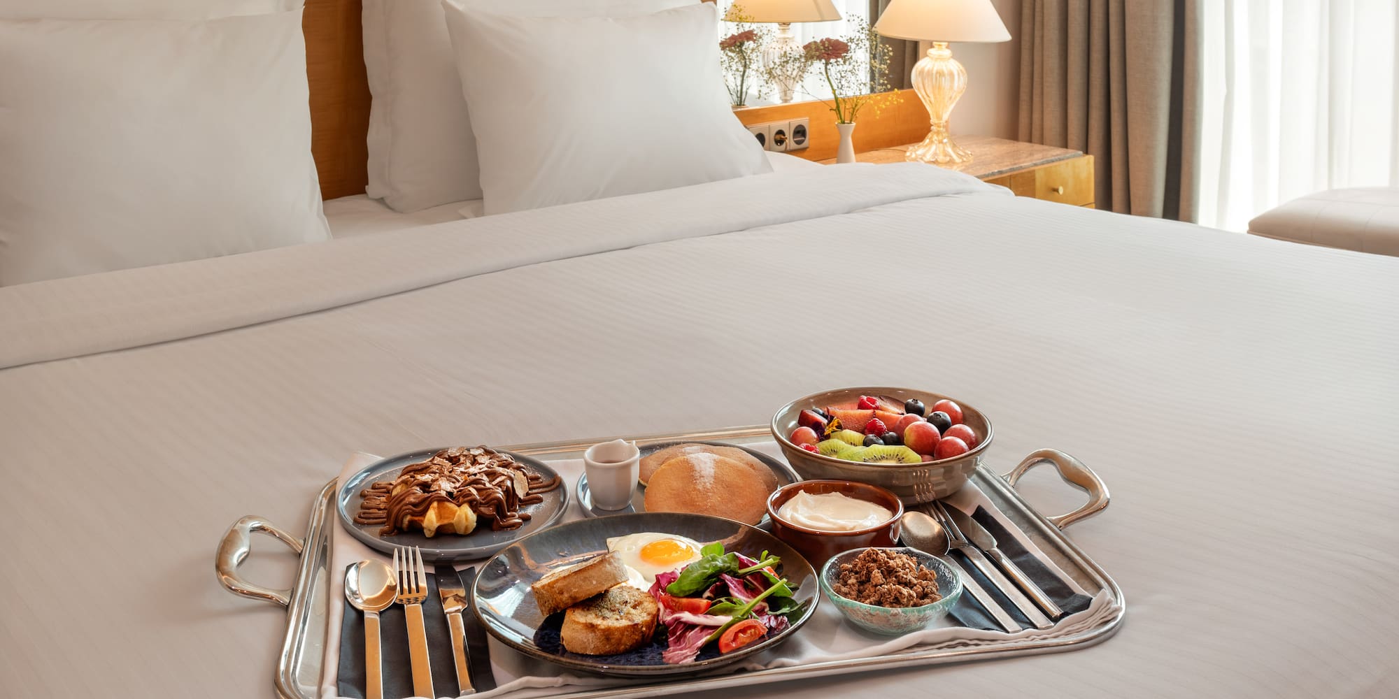 Hotel breakfast in bed with waffles, fruit, egg, and granola.