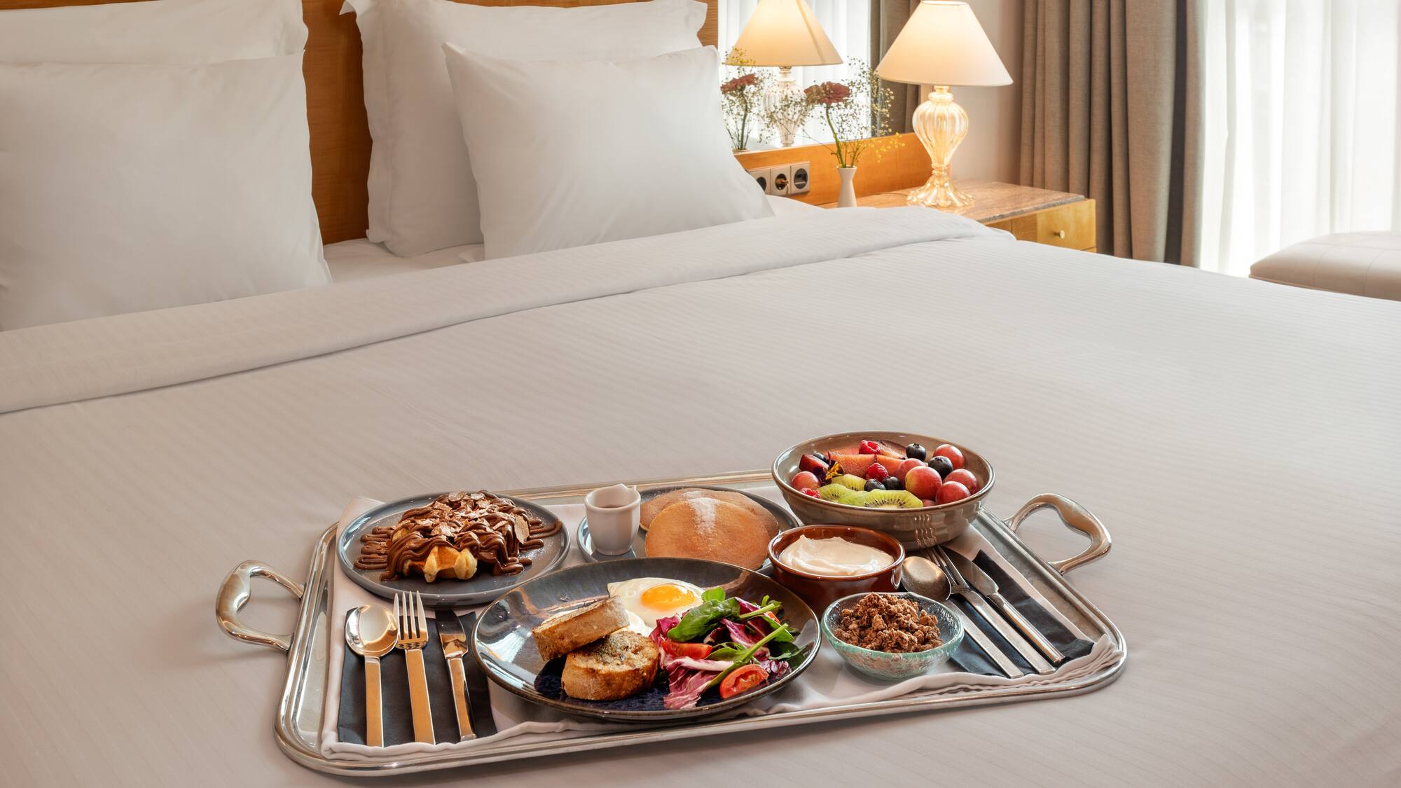Hotel breakfast in bed with waffles, fruit, egg, and granola.