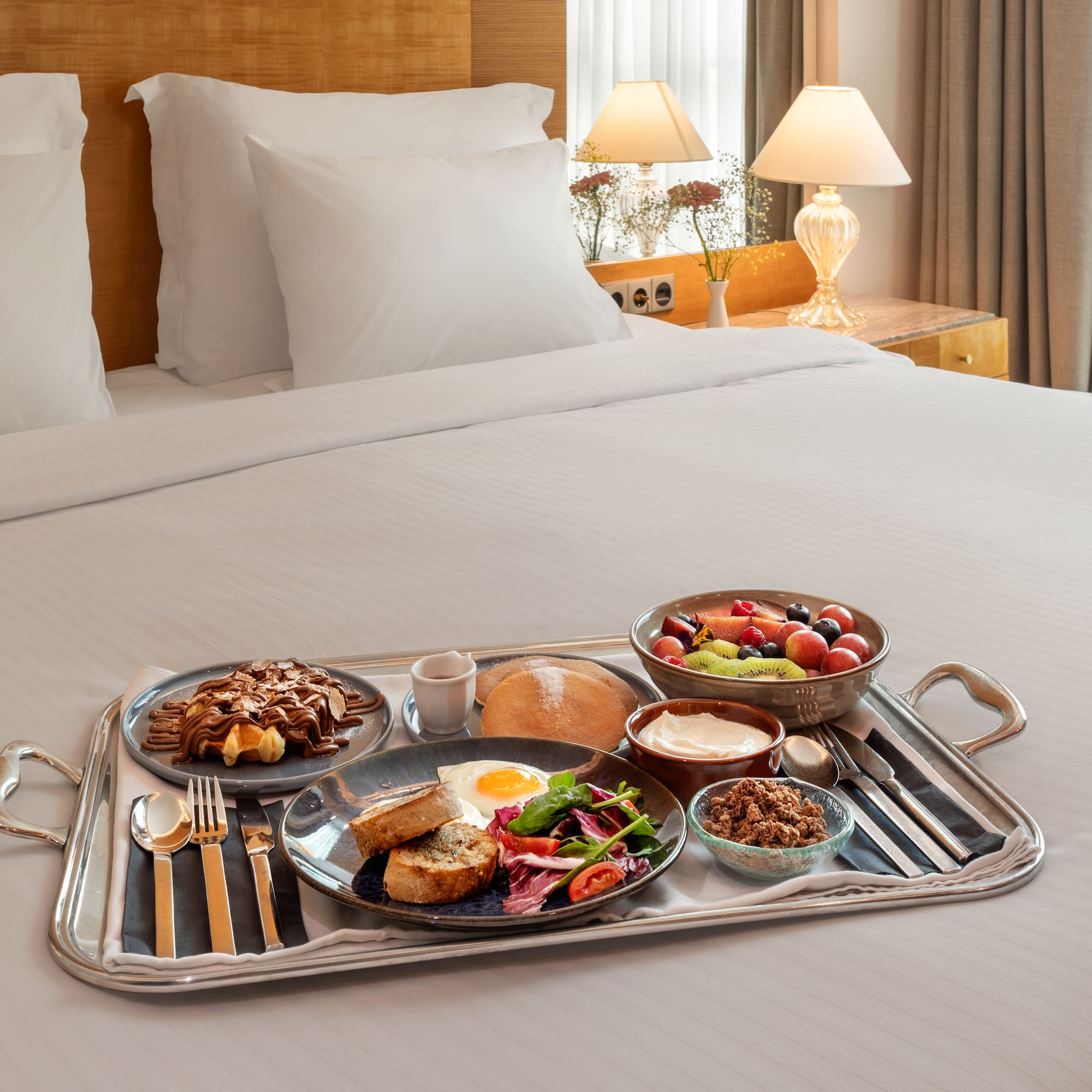 Hotel breakfast in bed with waffles, fruit, egg, and granola.