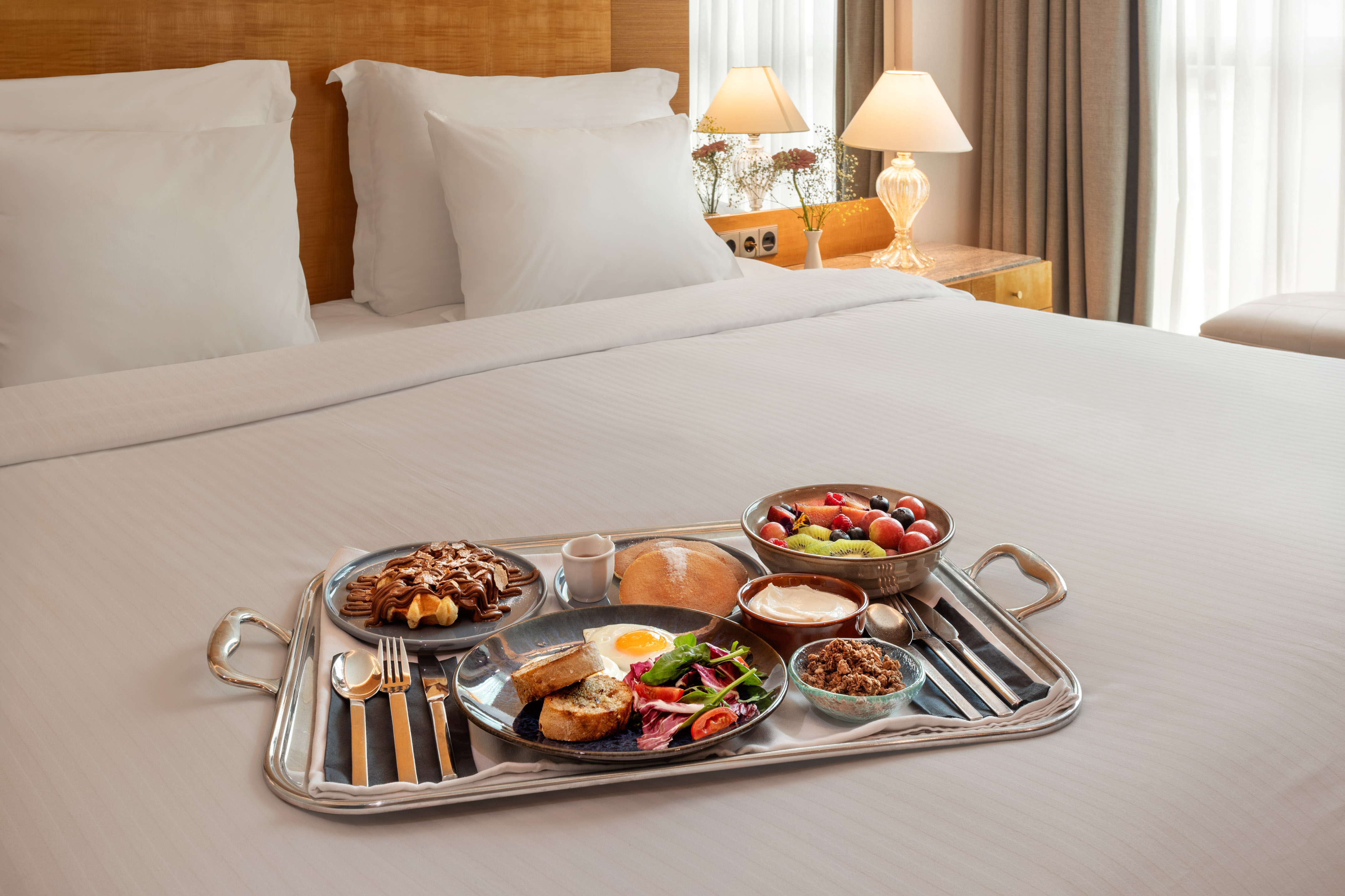 Hotel breakfast in bed with waffles, fruit, egg, and granola.