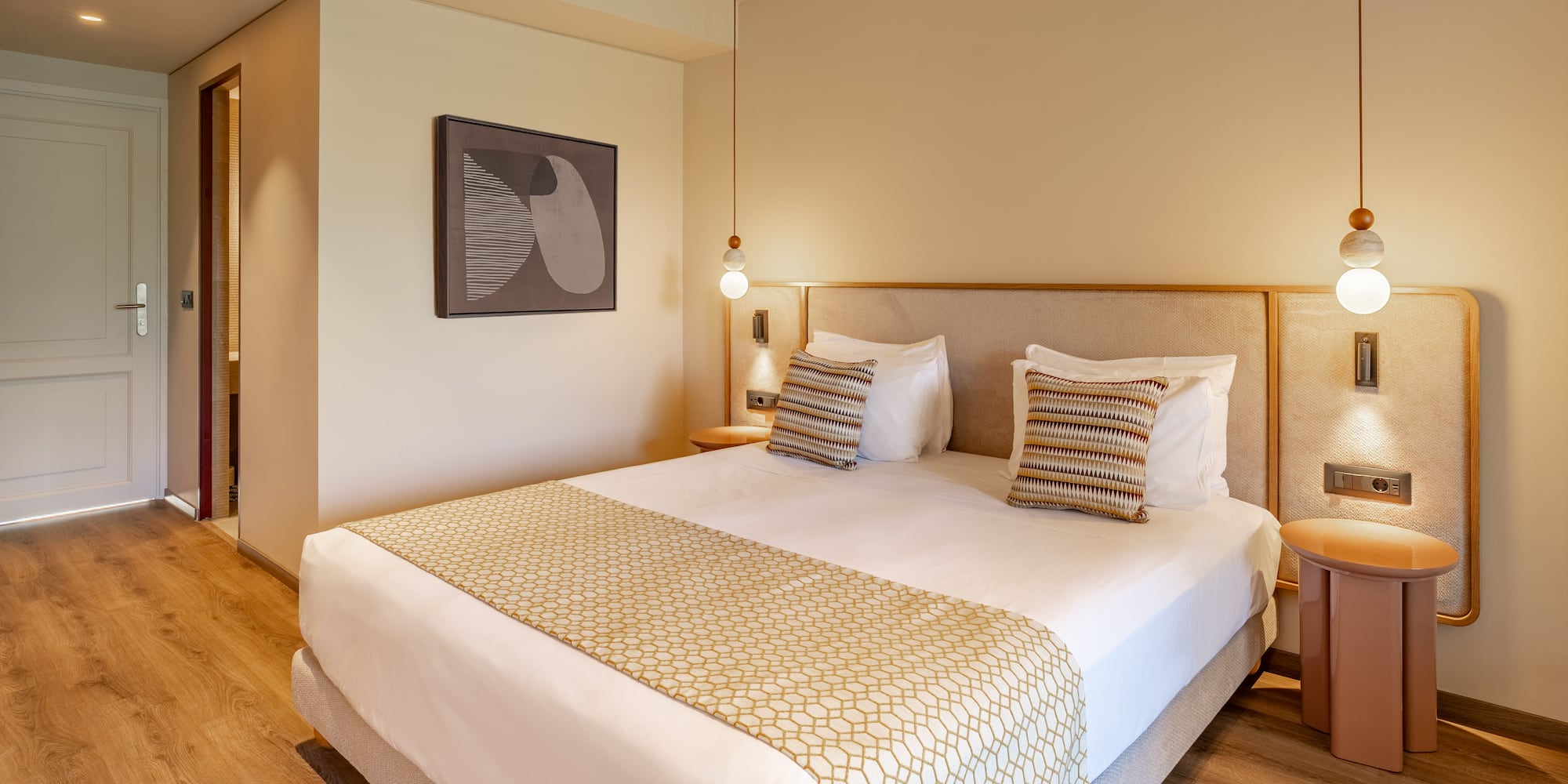 Modern hotel room with large bed, patterned runner, wood floor, and pendant lights.